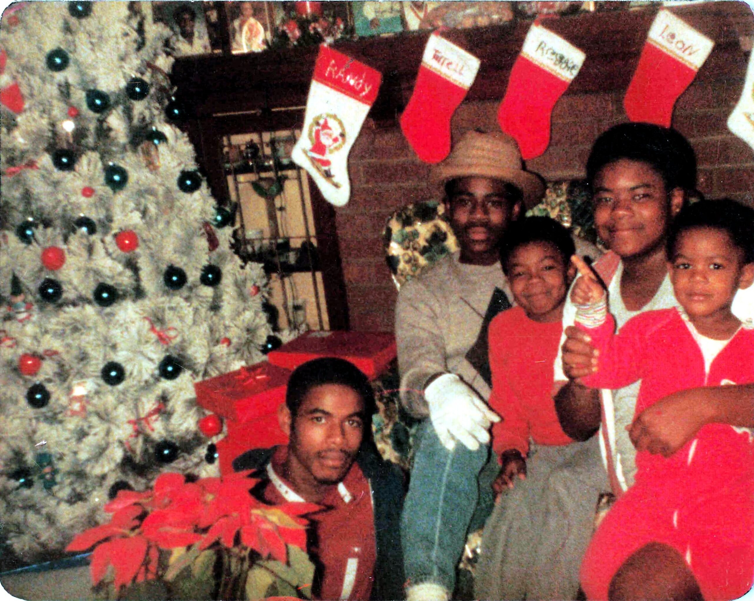 Family posing for a Christmas photo beside a white, ornamented tree with red and green decorations and stockings overhead.