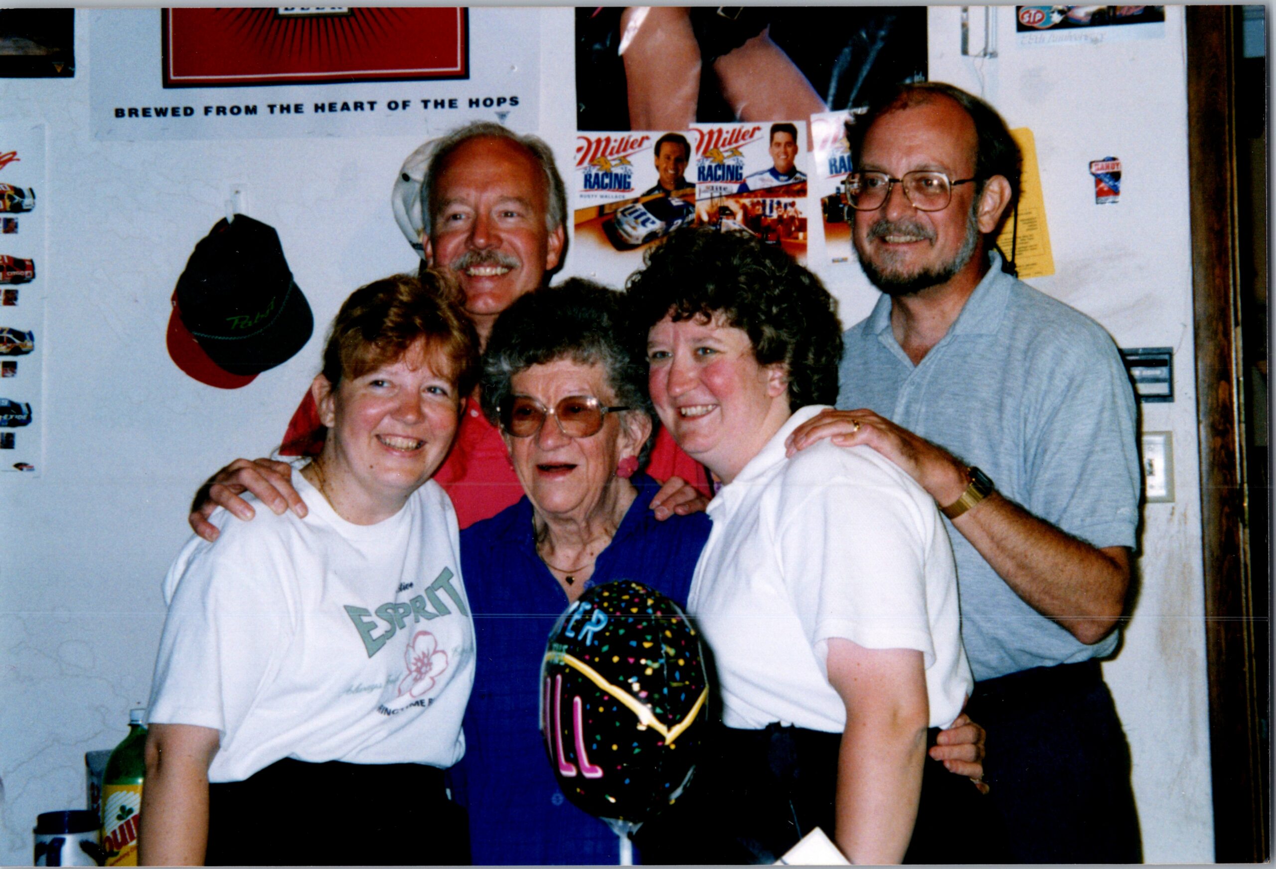 Five people pose together indoors, smiling at the camera with wall posters in the background.