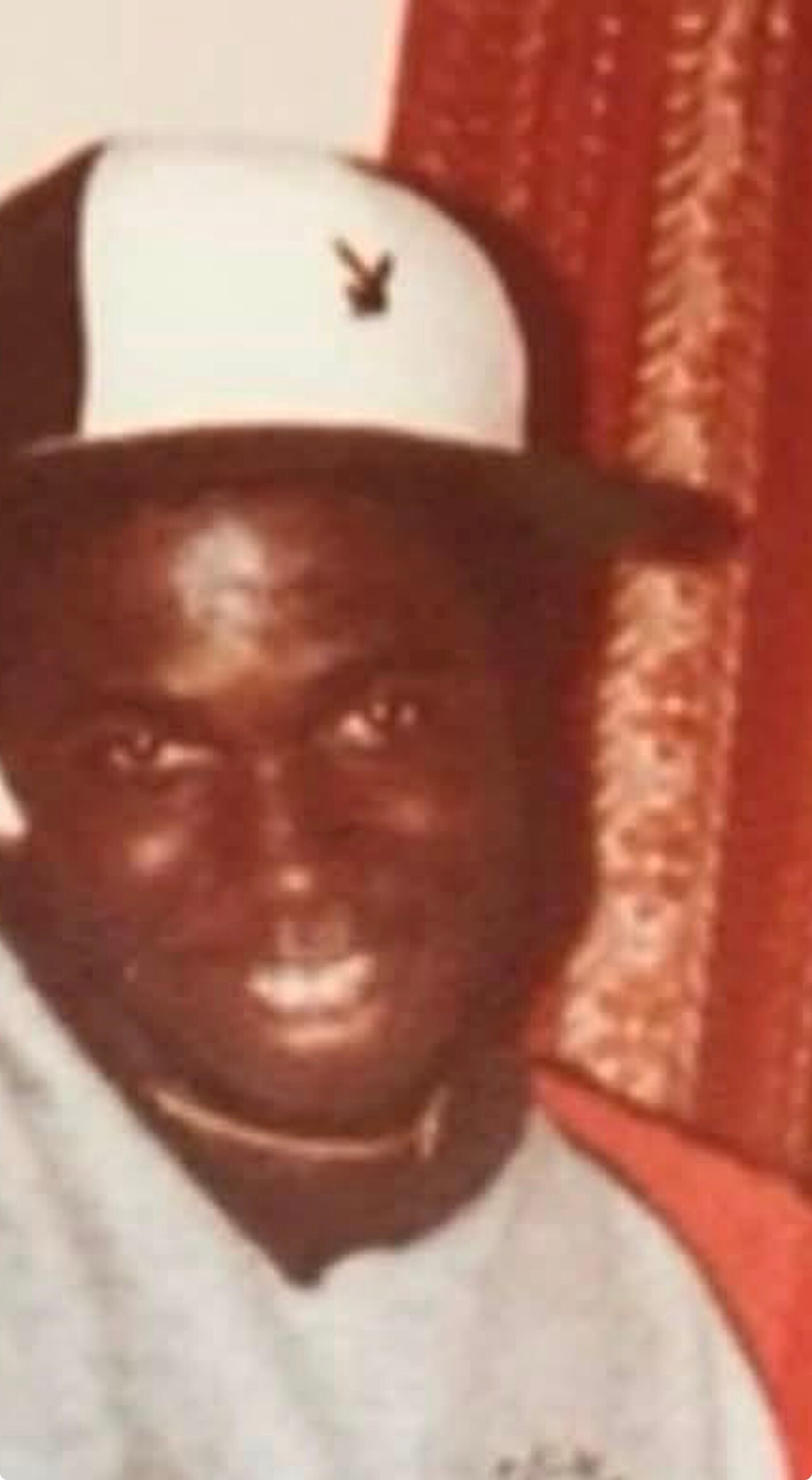 Man wearing a white baseball cap with a small black logo, facing forward in a close-up portrait.