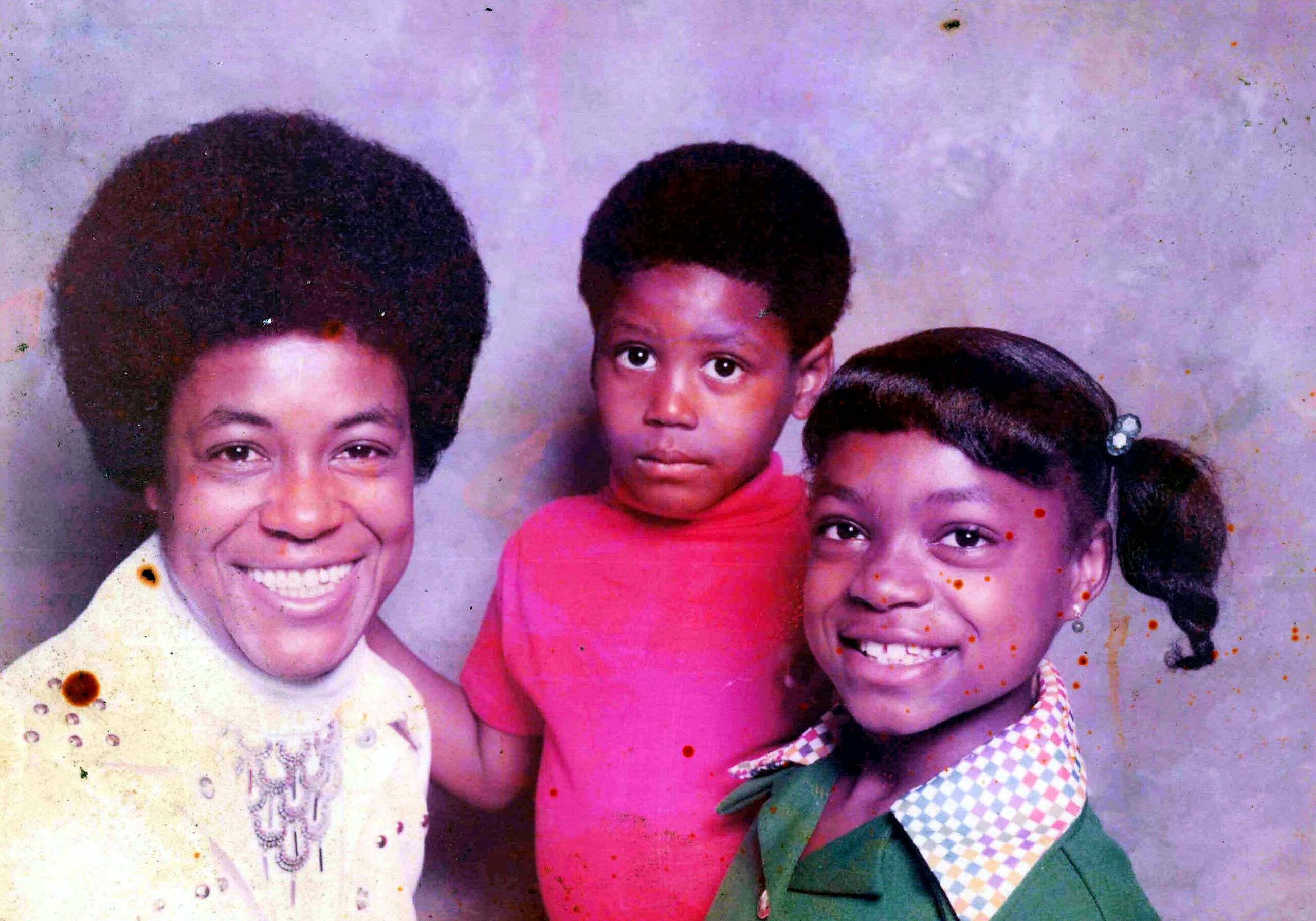 Three smiling children posing together for a studio portrait, with a purple backdrop behind them.
