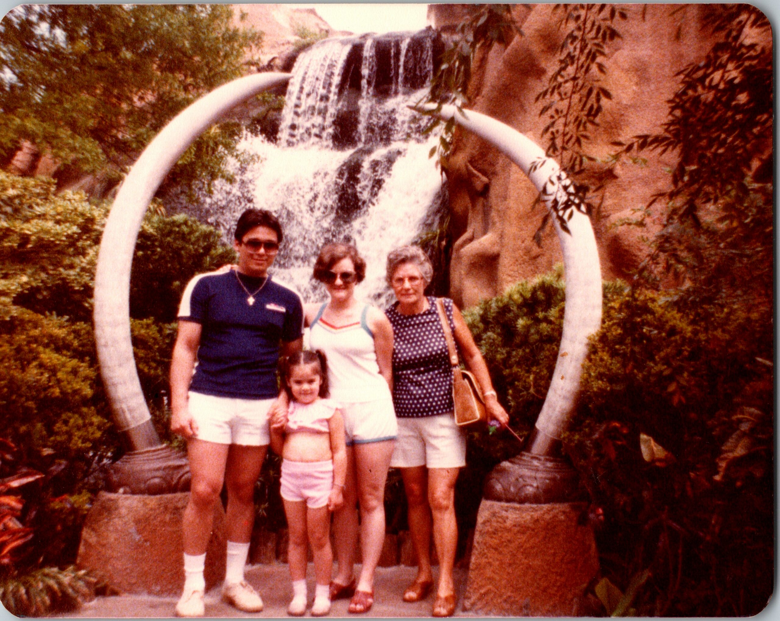 Family of five posing in front of a curved white arch with a cascading waterfall in a lush garden.