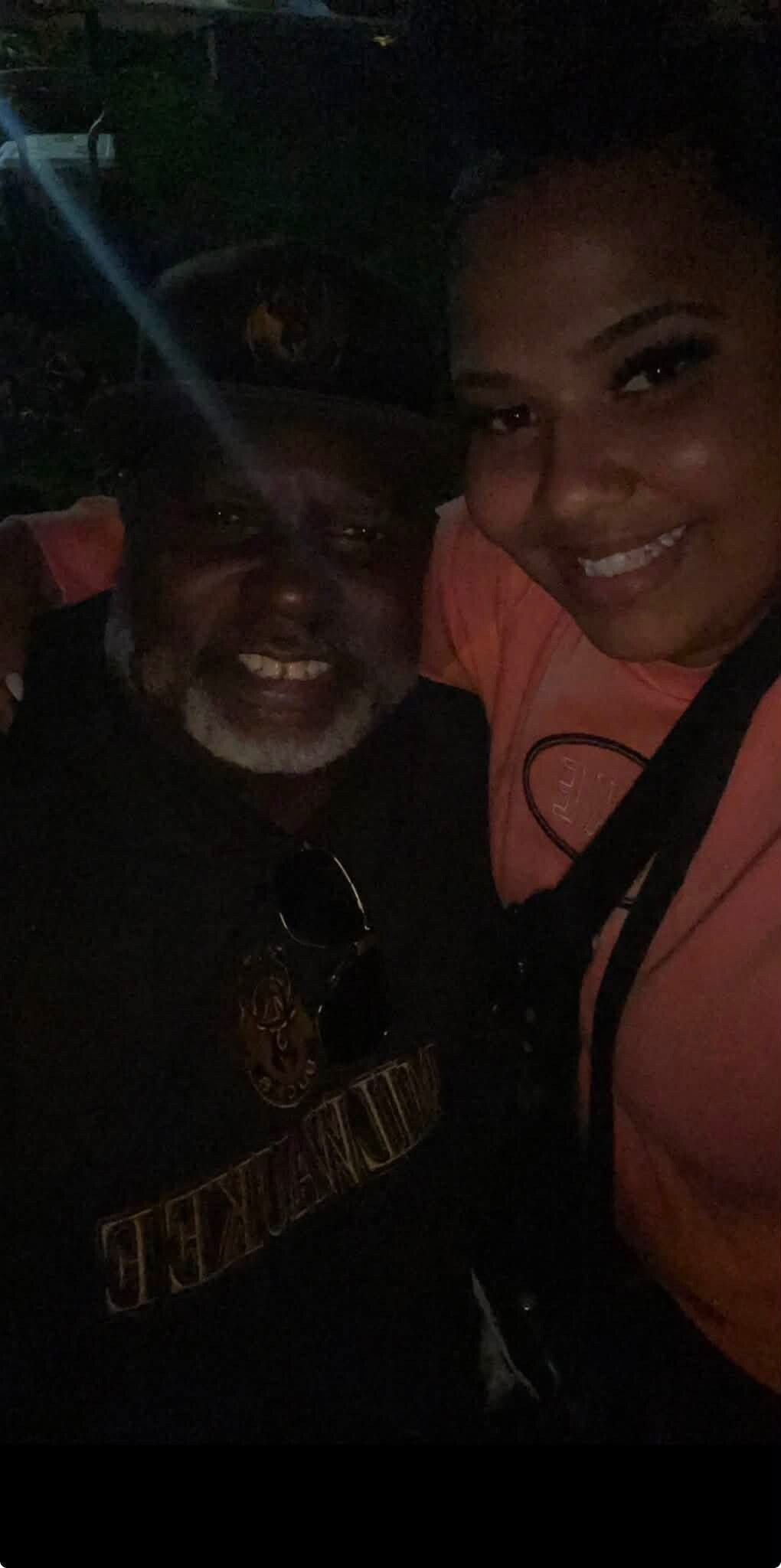 Two people smiling for a selfie at night; a man with a gray beard on the left and a woman in a pink jacket on the right.