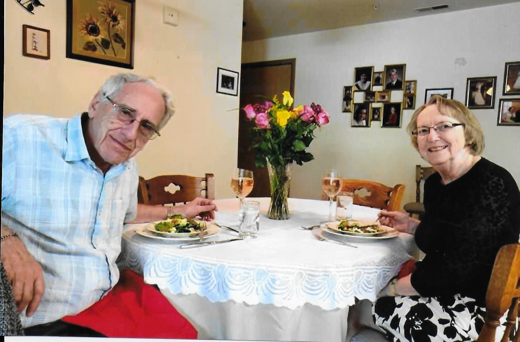 Elderly couple dining at a table with a flower vase, enjoying their meals and drinks at a homey restaurant setting.