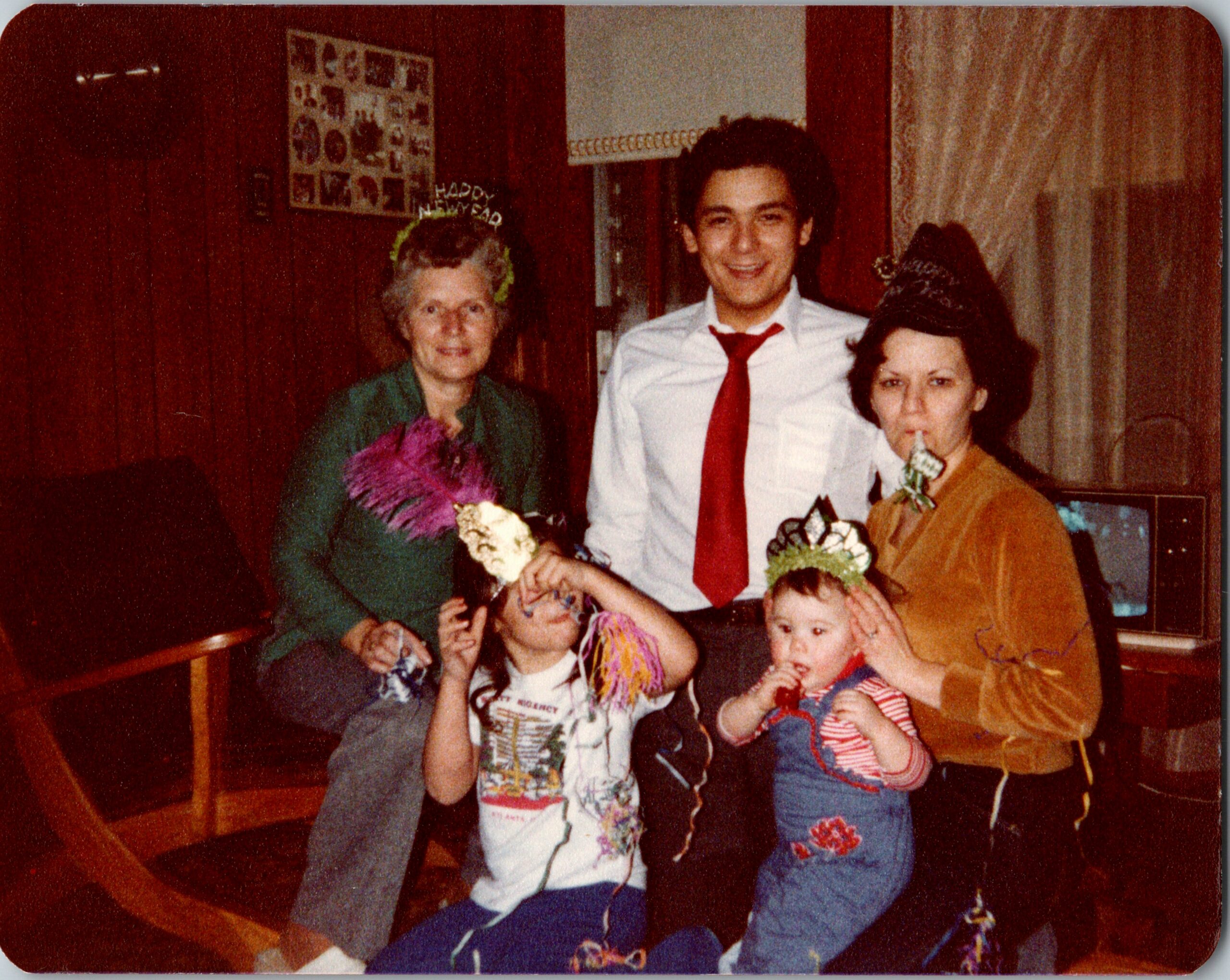 Group of people at a birthday party posing for a photo, with party hats and confetti streamer decorations.