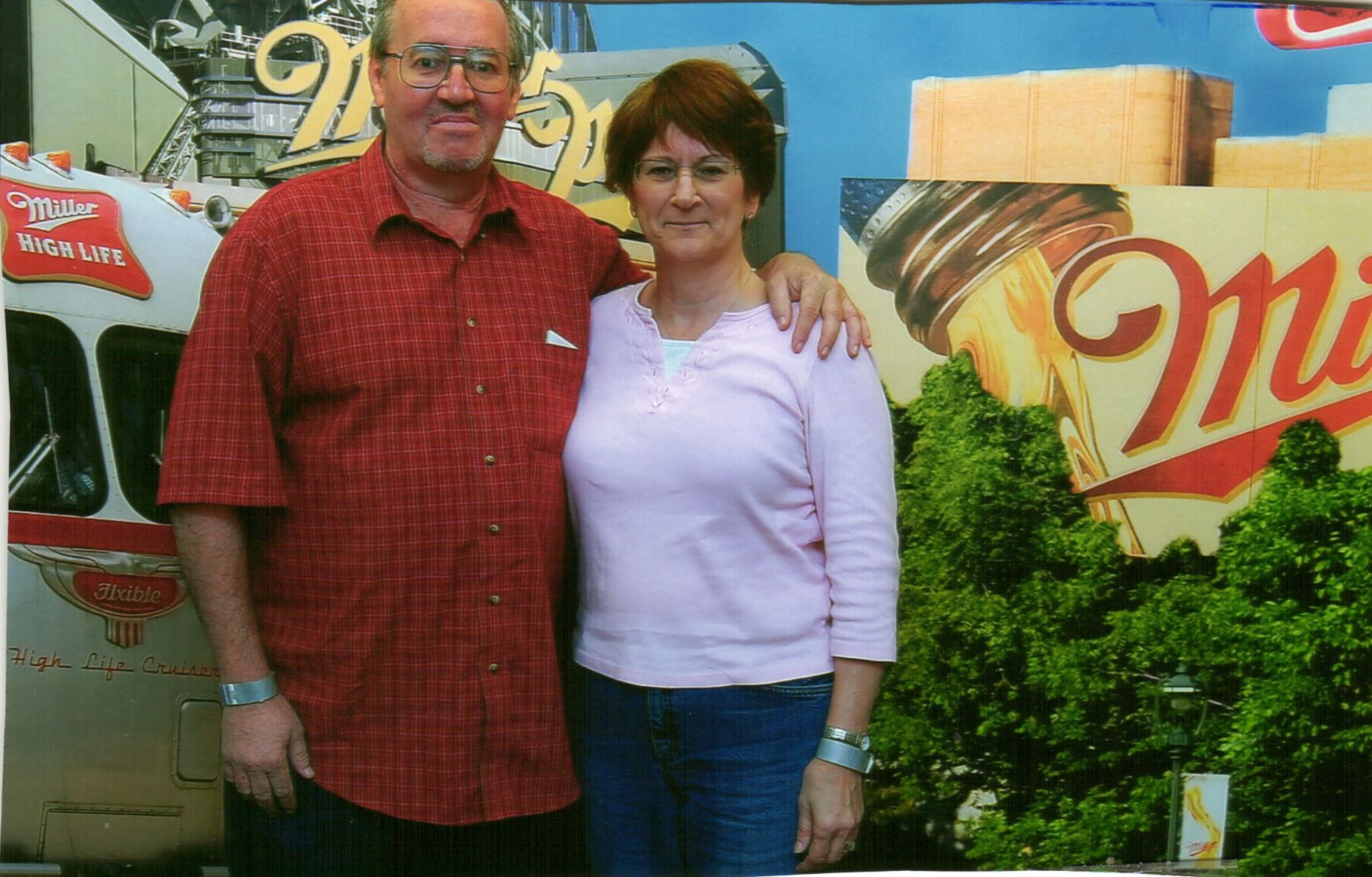 Couple posing with arms around each other in front of a colorful Miller High Life backdrop.