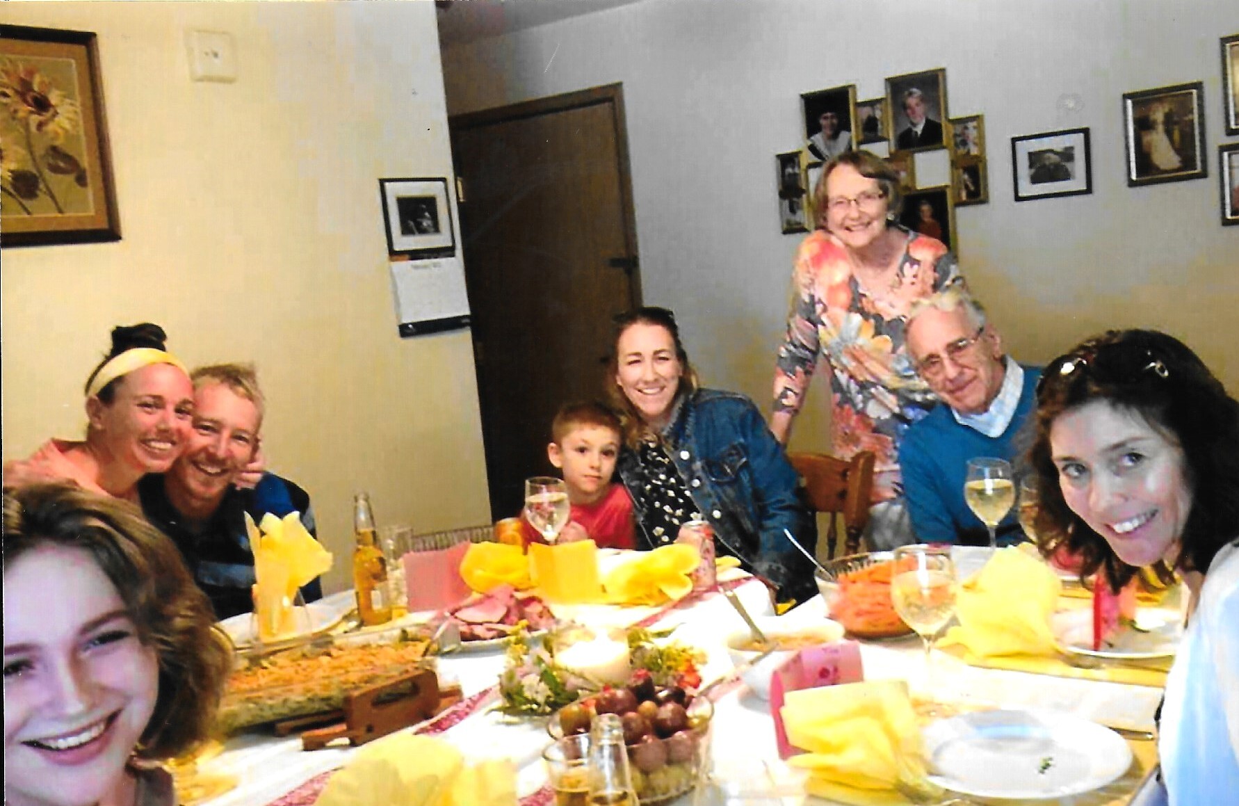 Smiling group around a dinner table with yellow napkins and drinks during a celebration.