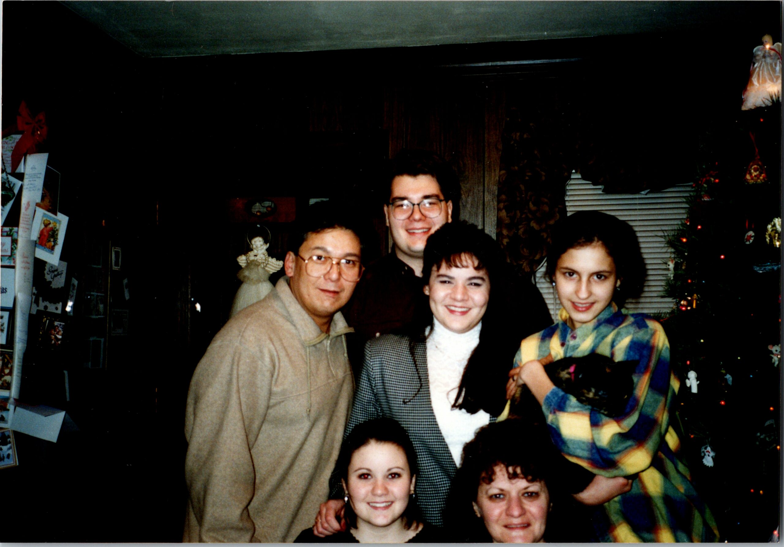 Group of people posing for a festive indoor photo, smiling faces, Christmas tree and decorations in background.