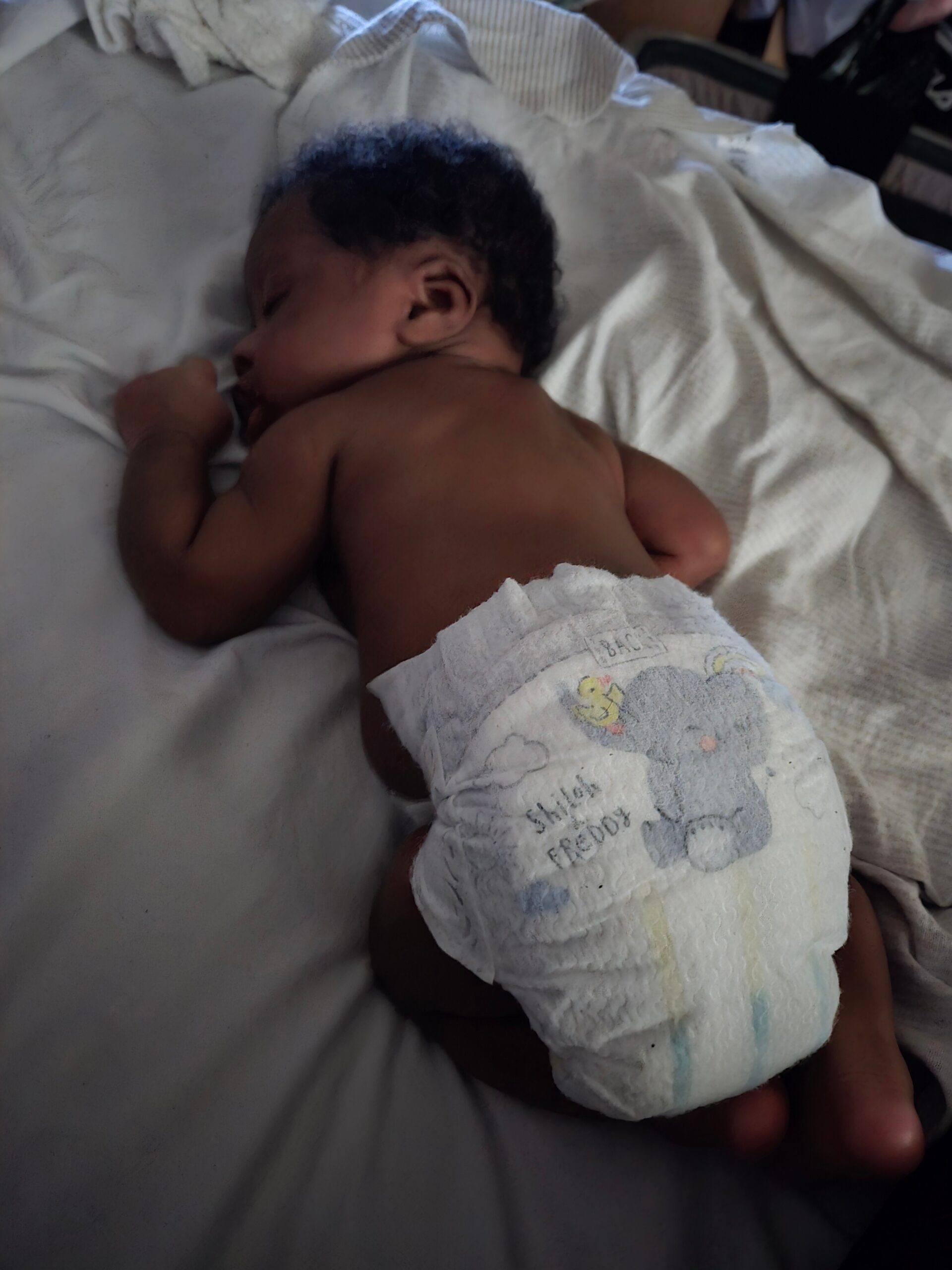 Newborn baby sleeping on a hospital bed, wearing a Winnie the Pooh diaper printed with characters and clouds.