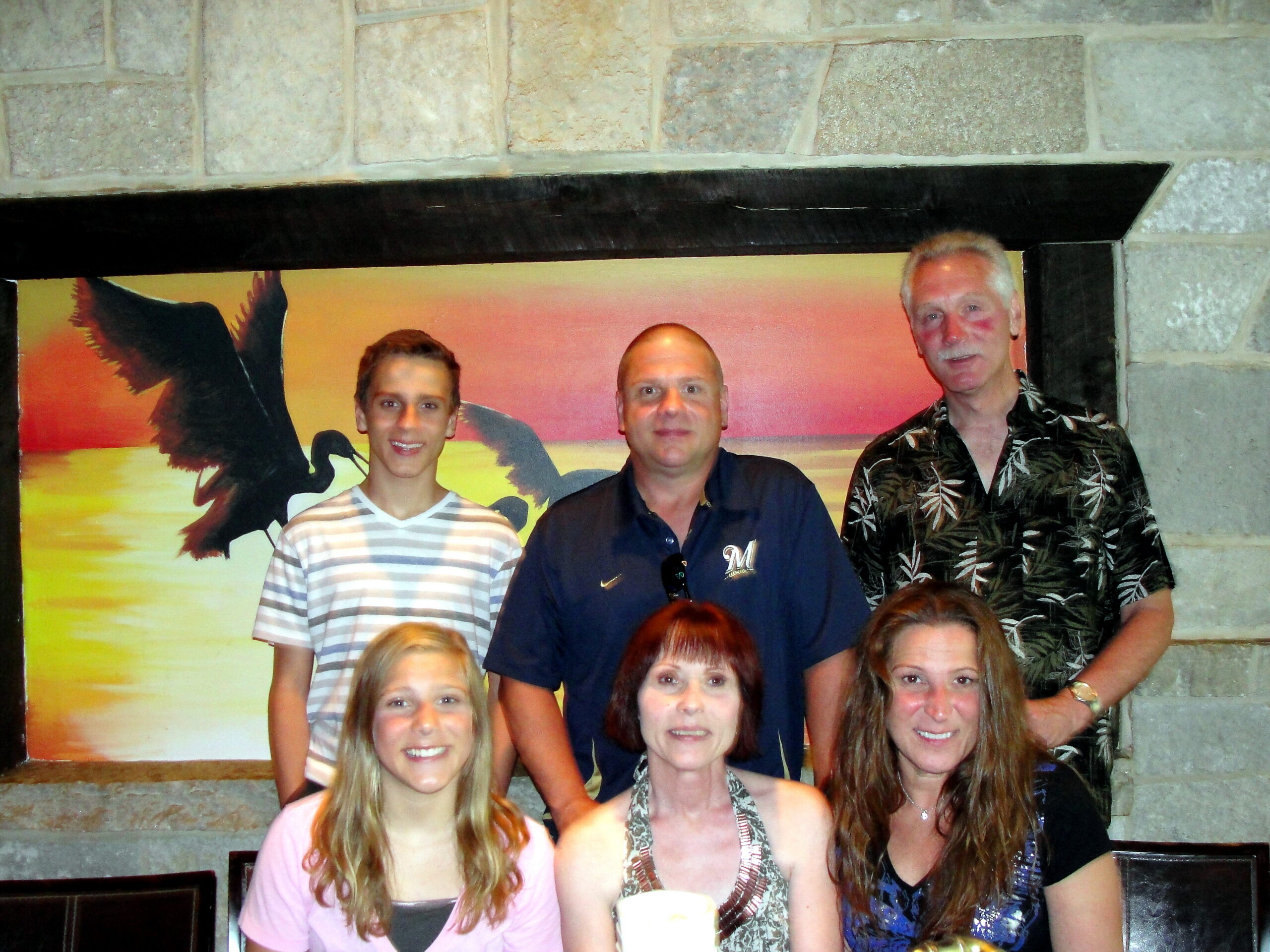 Group of people posing together in front of a sunset mural with birds inside a stone-framed display.