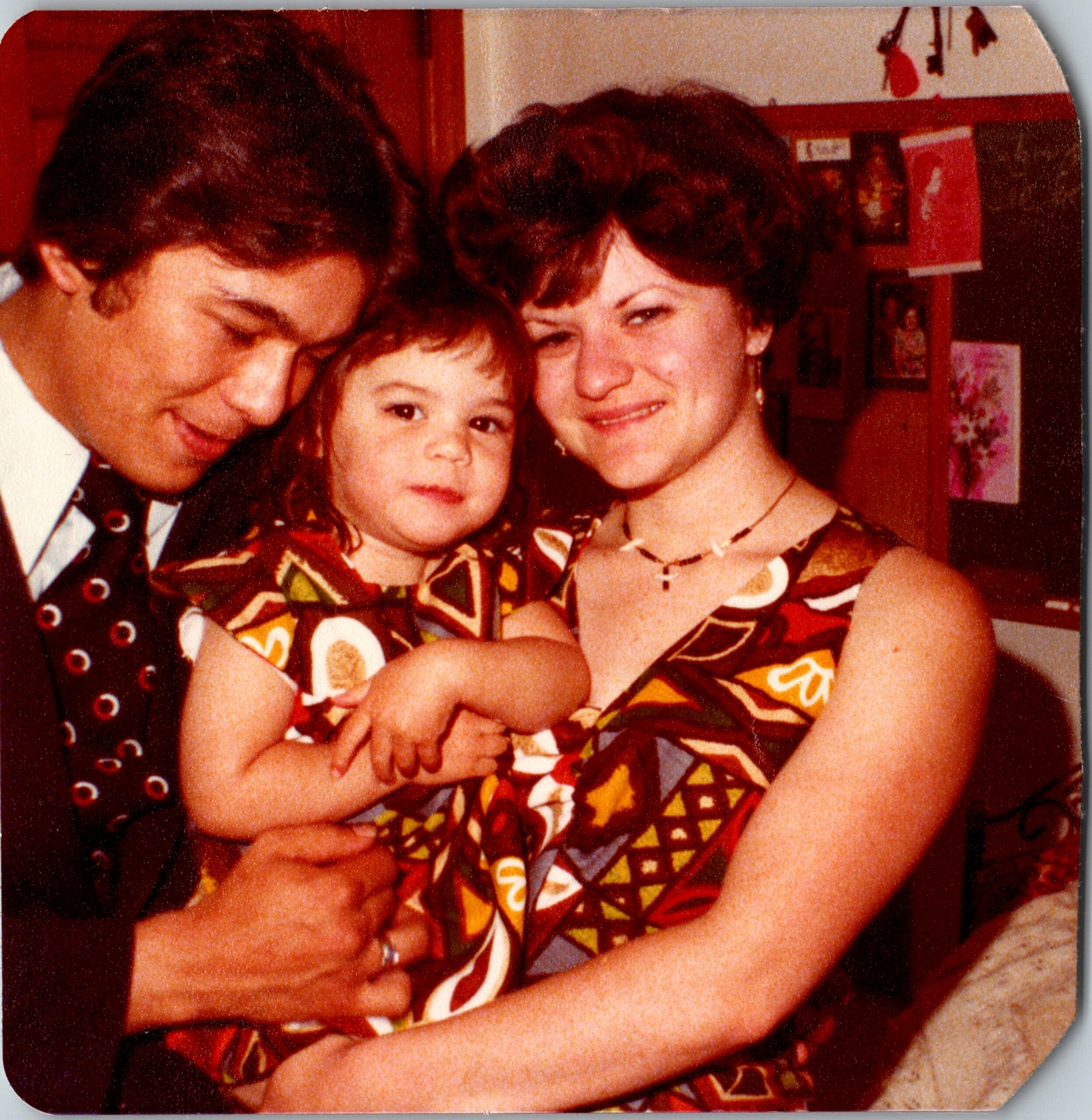 A smiling family portrait with a man, a woman, and a young child close together in colorful clothing.