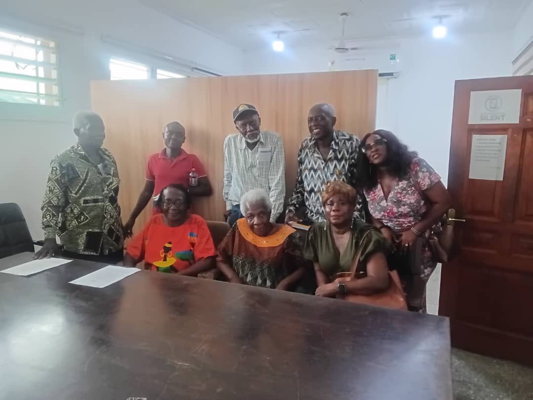 Eight adults posing for a group photo in a meeting room, some seated at a table with papers behind them.