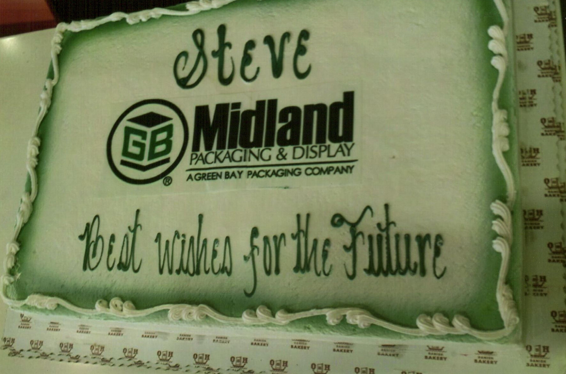 Green rectangular cake with white piping, featuring the Steve Midland Packaging & Display logo and slogan on top surface.