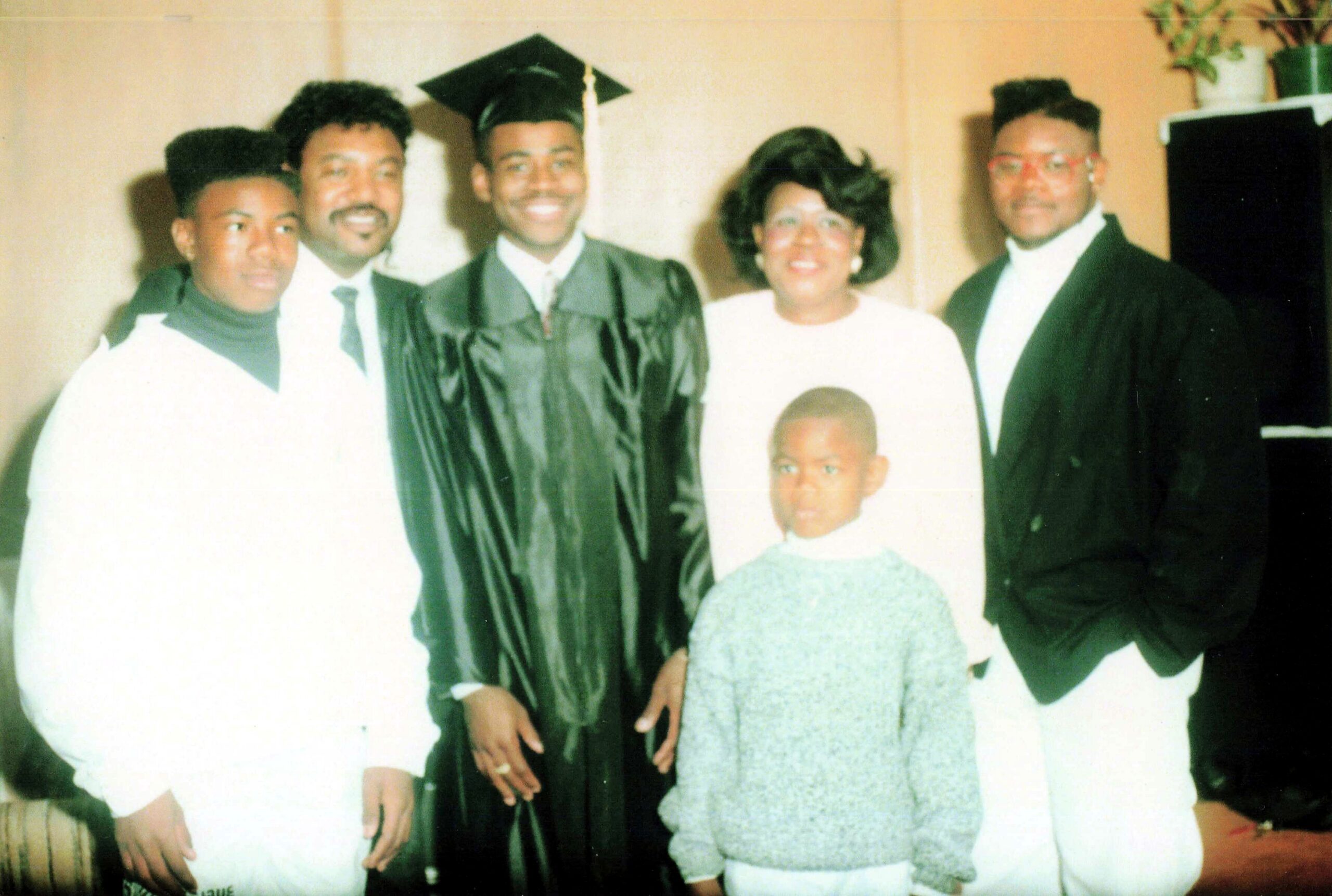 Group of five posing for a graduation photo: the graduate in a cap and gown surrounded by relatives in formal attire, with a child in front.