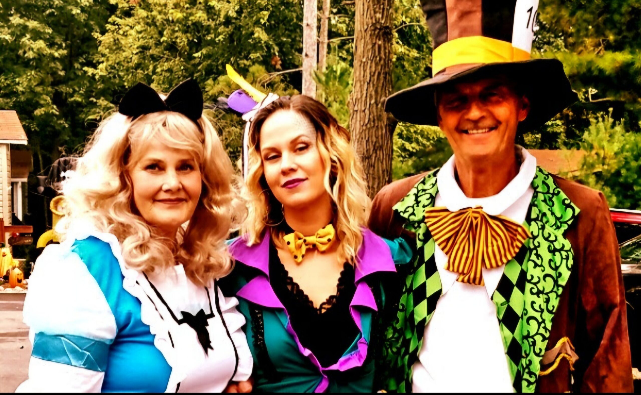 Three adults in bright carnival costumes posing outdoors, smiling at the camera.