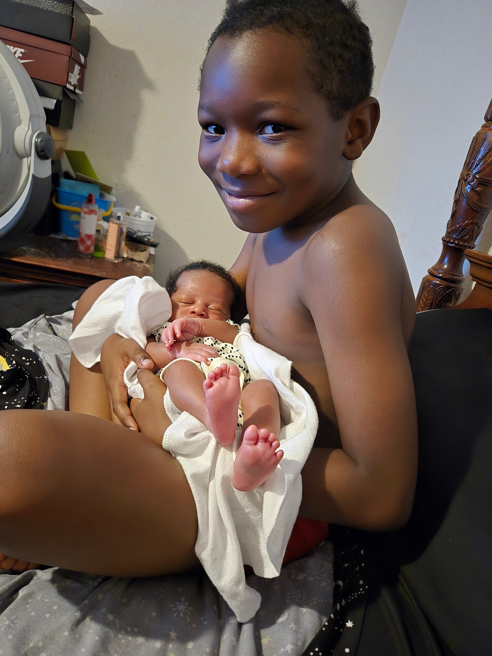 Young boy cradling a newborn baby wrapped in a white towel, smiling at the camera.