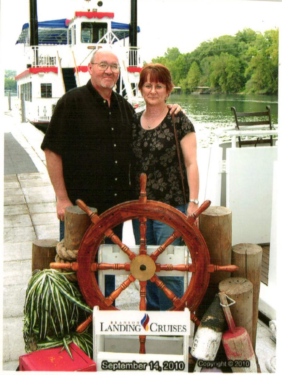 Couple posing on a dock beside a large wooden ship's wheel, with a Branson Landing Cruises sign and the date September 14, 2010 visible.