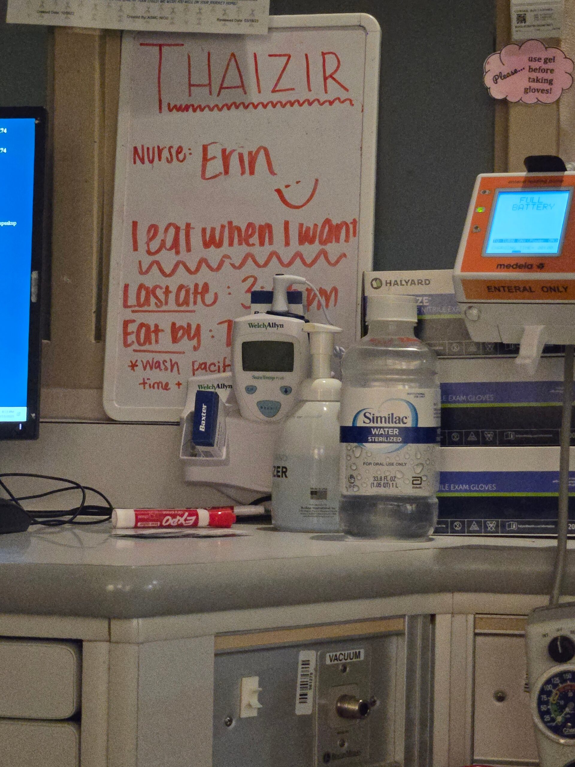 Whiteboard with red handwriting reading 'Nurse Erin' and a smiley, listing feeding and wash times in a hospital desk area.