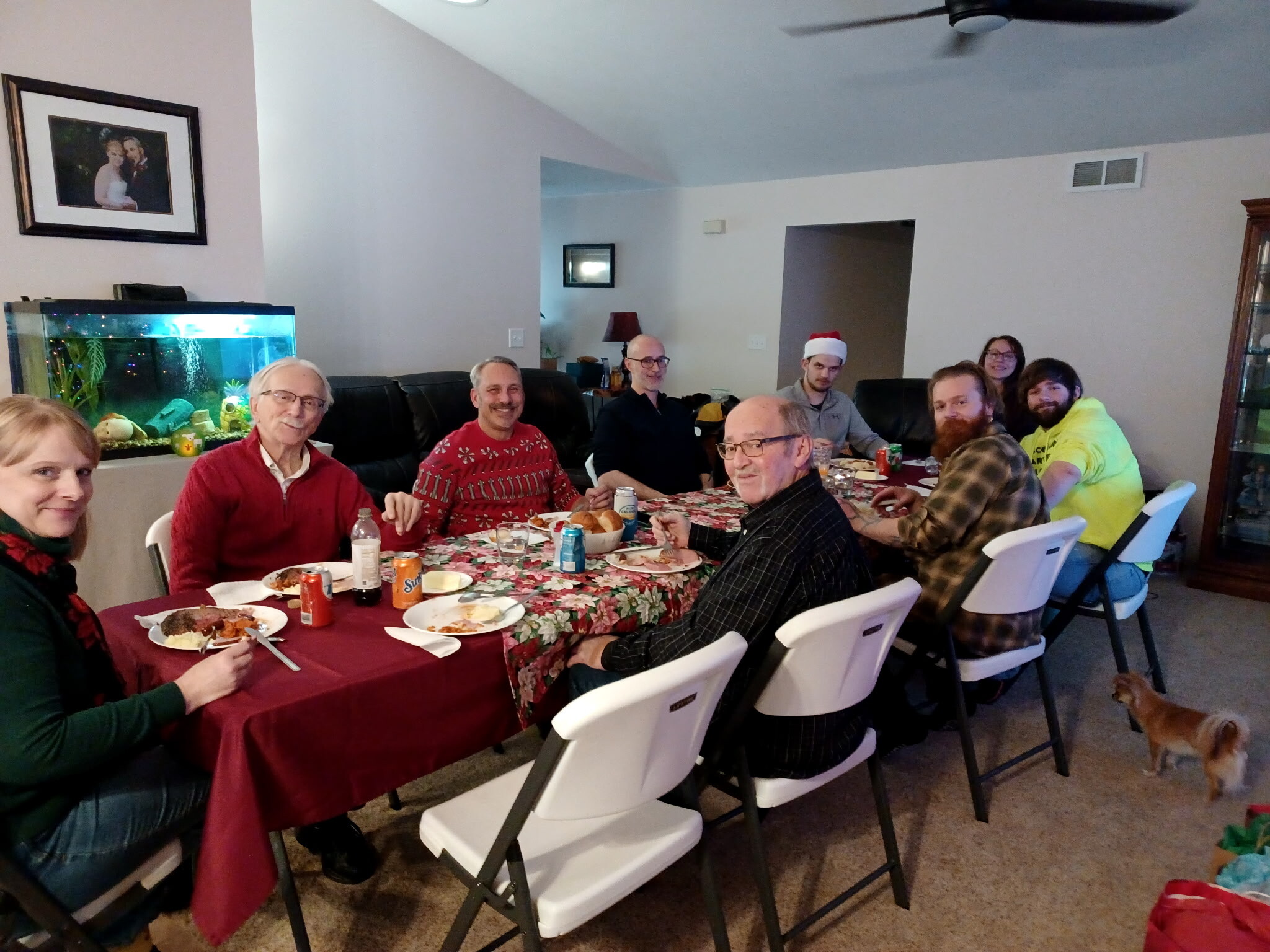 Group of people around a long table enjoying a Christmas meal in a living room, smiling at the camera.