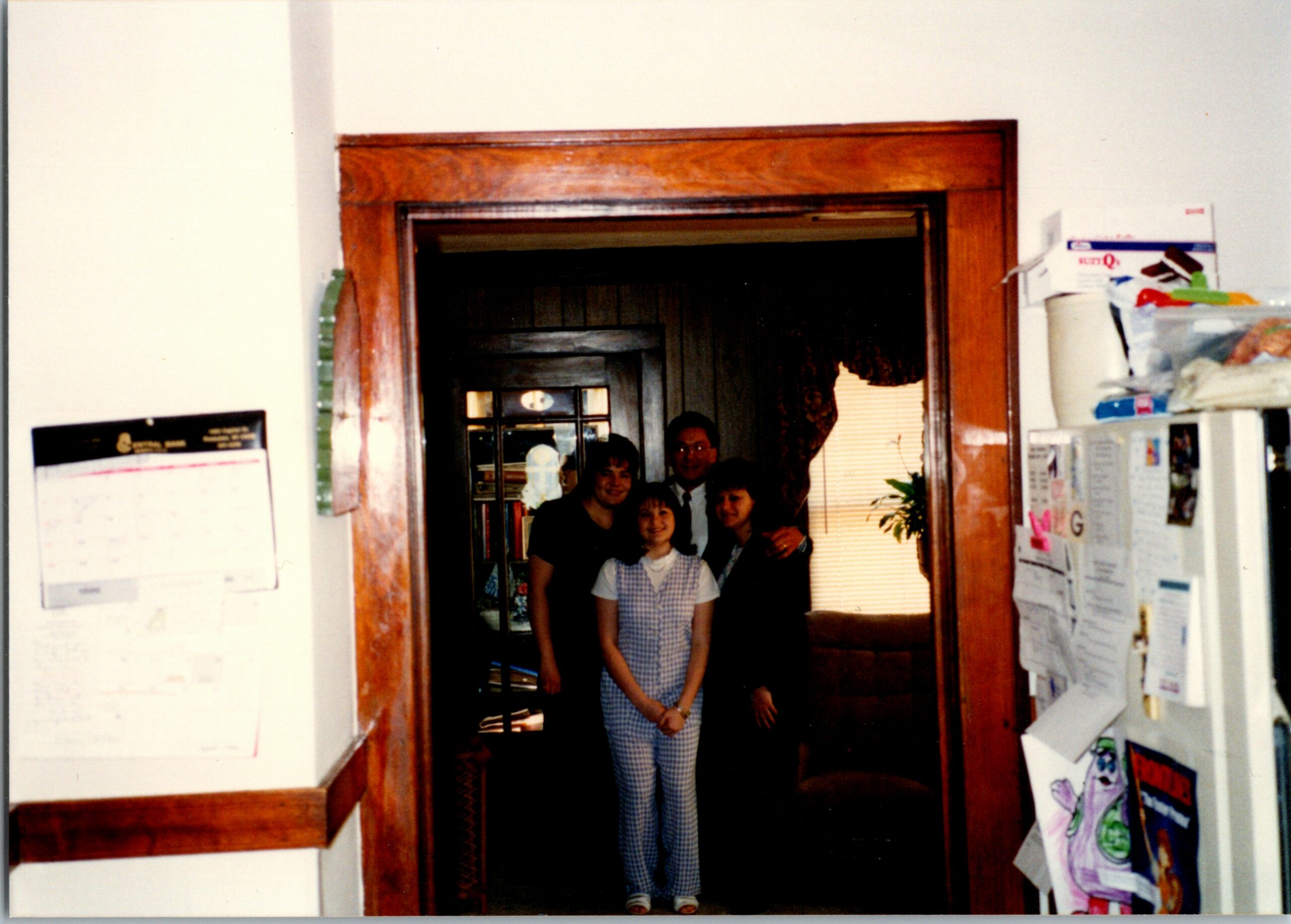 Family group posing in a wood-framed doorway between rooms, smiling at the camera inside a home.