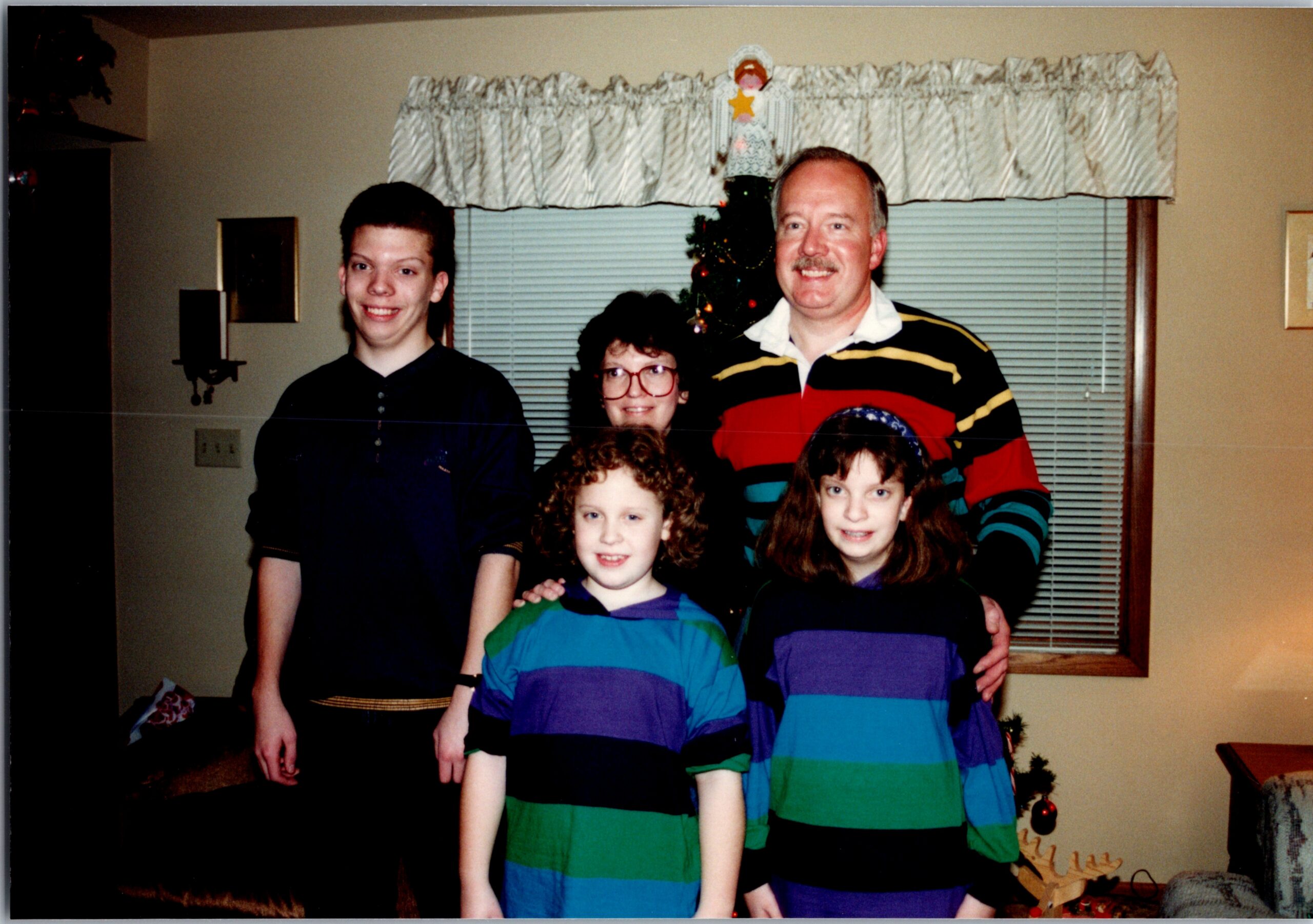 Family group posing for a photo in a living room with a Christmas tree in the background and striped shirts on several children and adults, smiling at the camera.