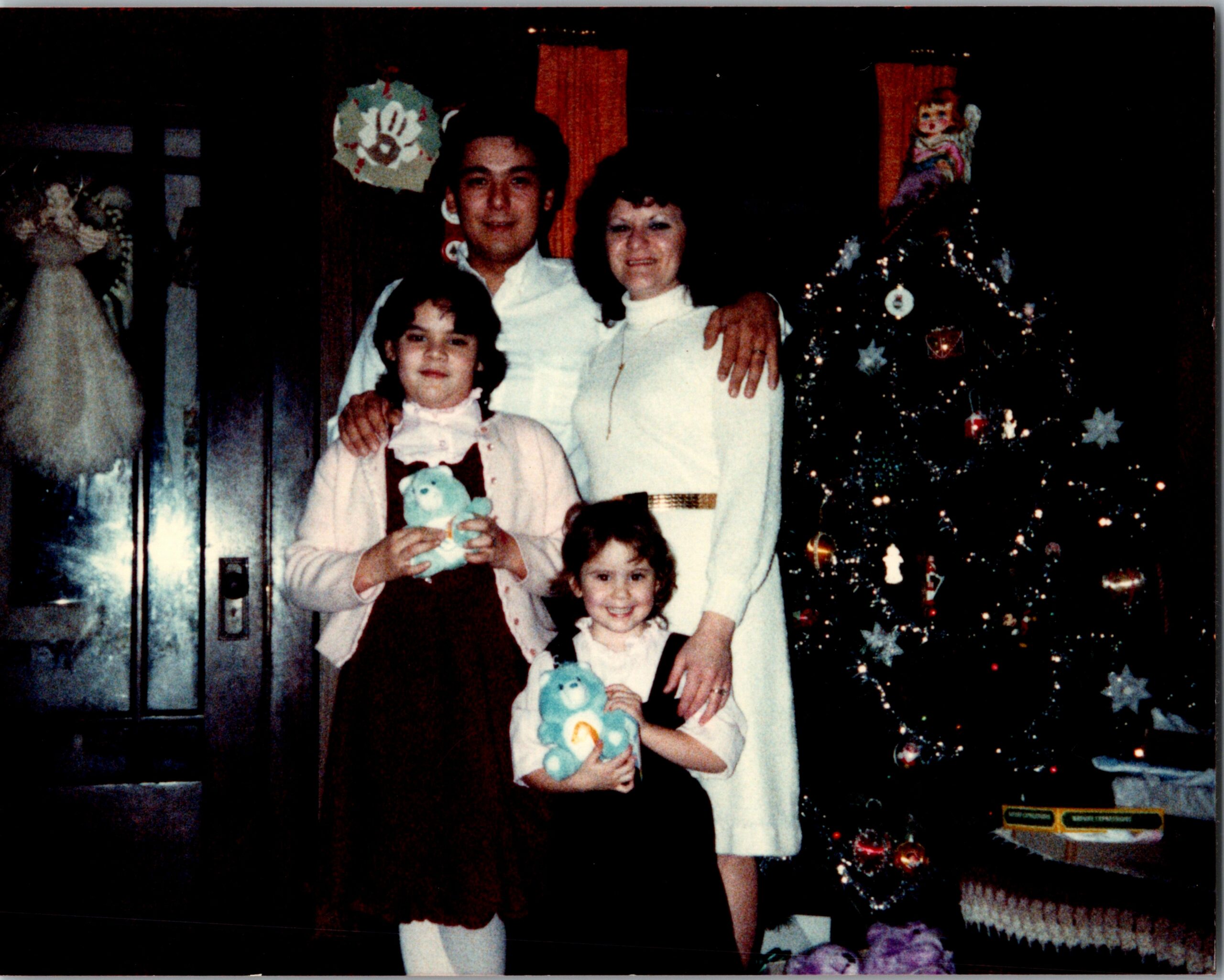 Family posing for a Christmas photo indoors: a man, a woman, and two children stand in front of a decorated Christmas tree.