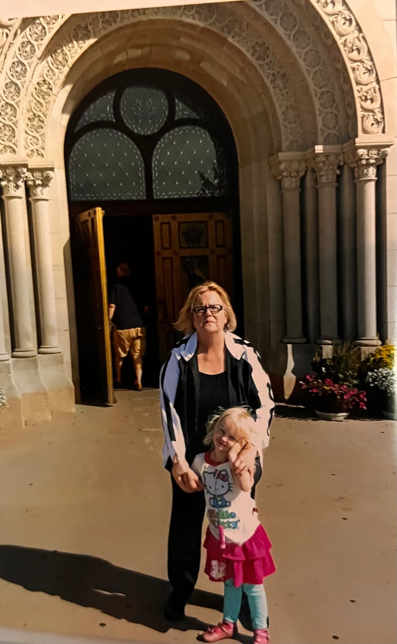 Woman and young girl pose together outside a stone building with an ornate arched doorway and columns.