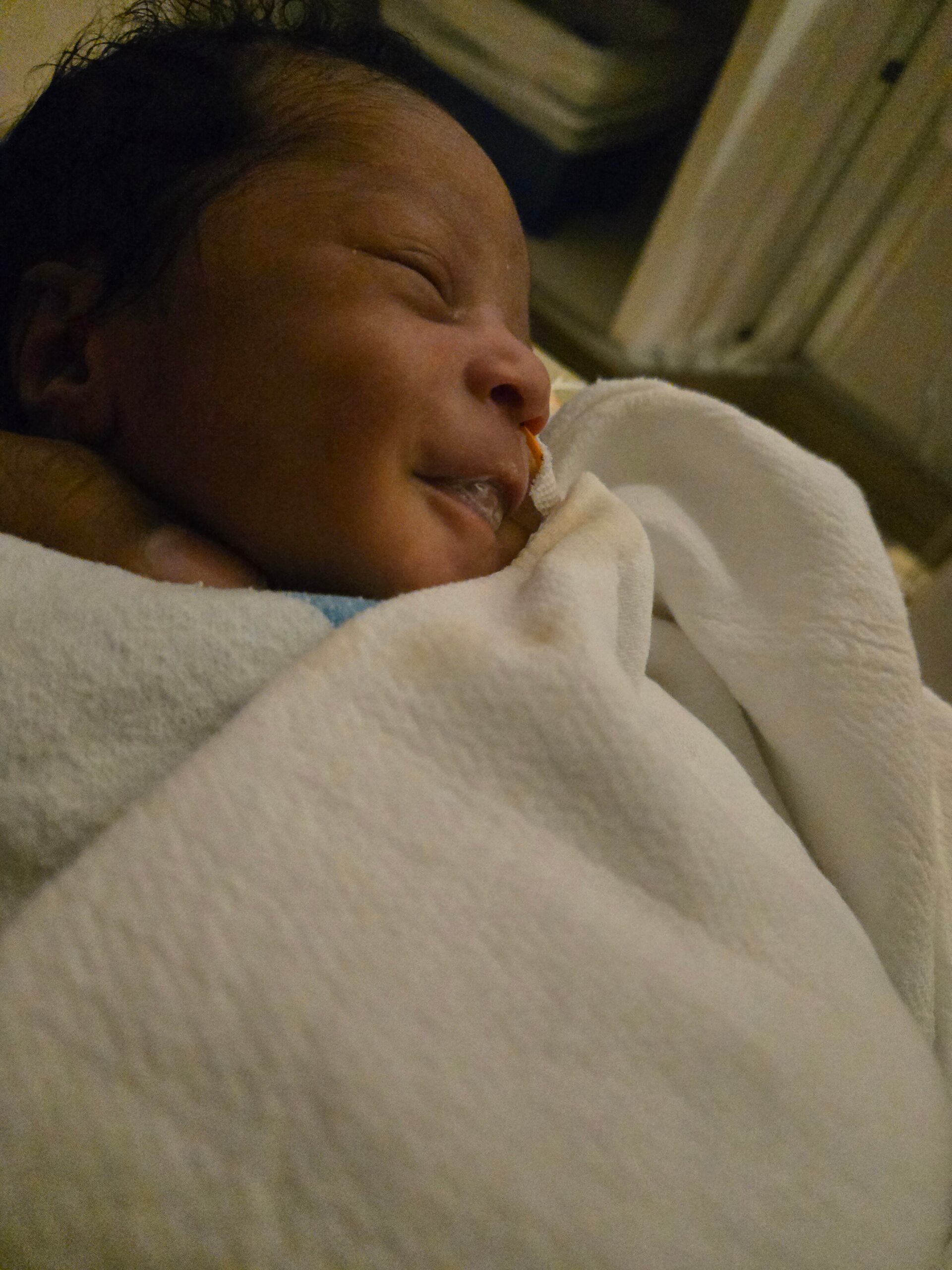 Close-up of a newborn baby sleeping, wrapped in a white blanket with a calm, peaceful expression.