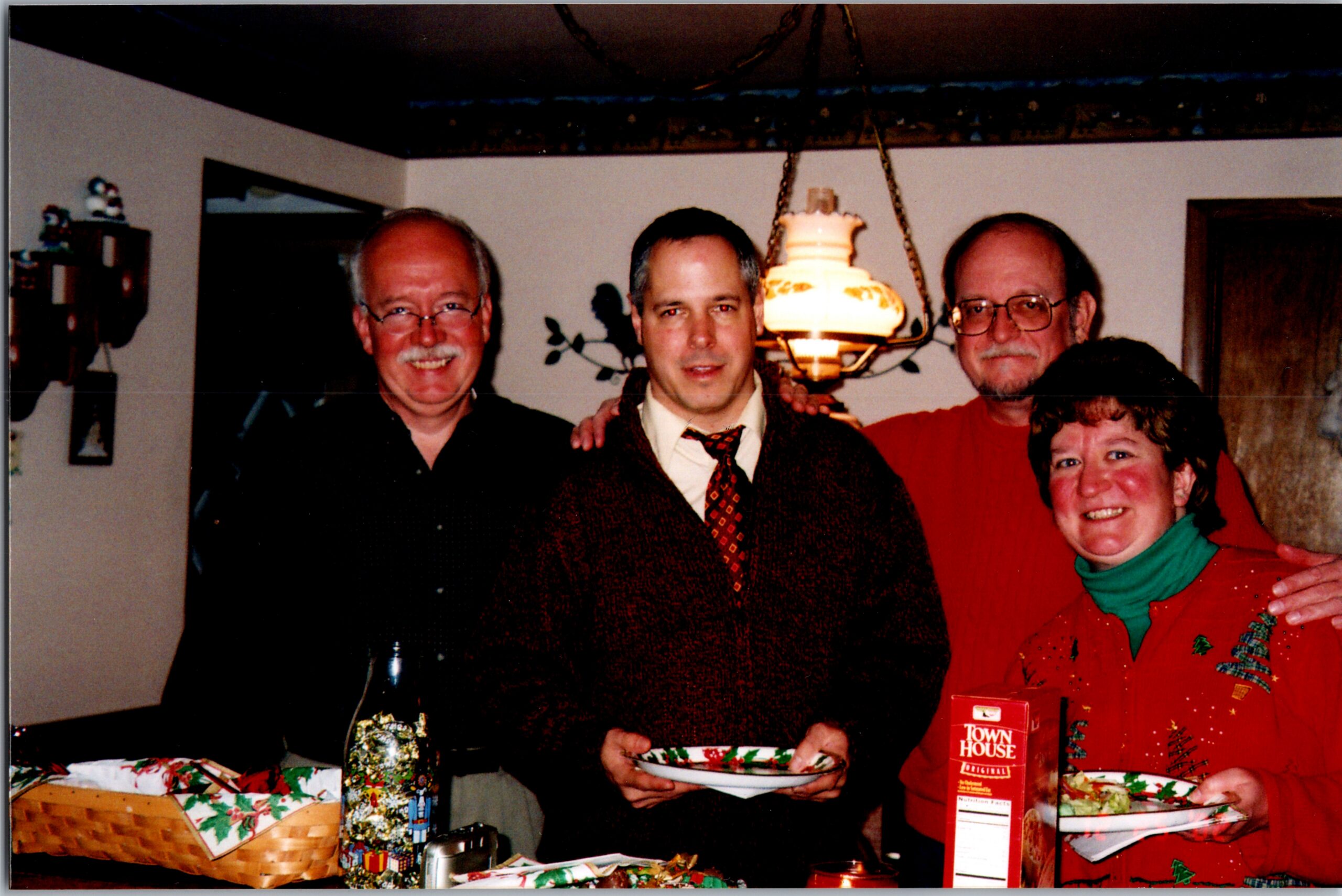 A group of four adults smiling around a table with wrapped Christmas gifts, posing for a photo at a holiday gathering.