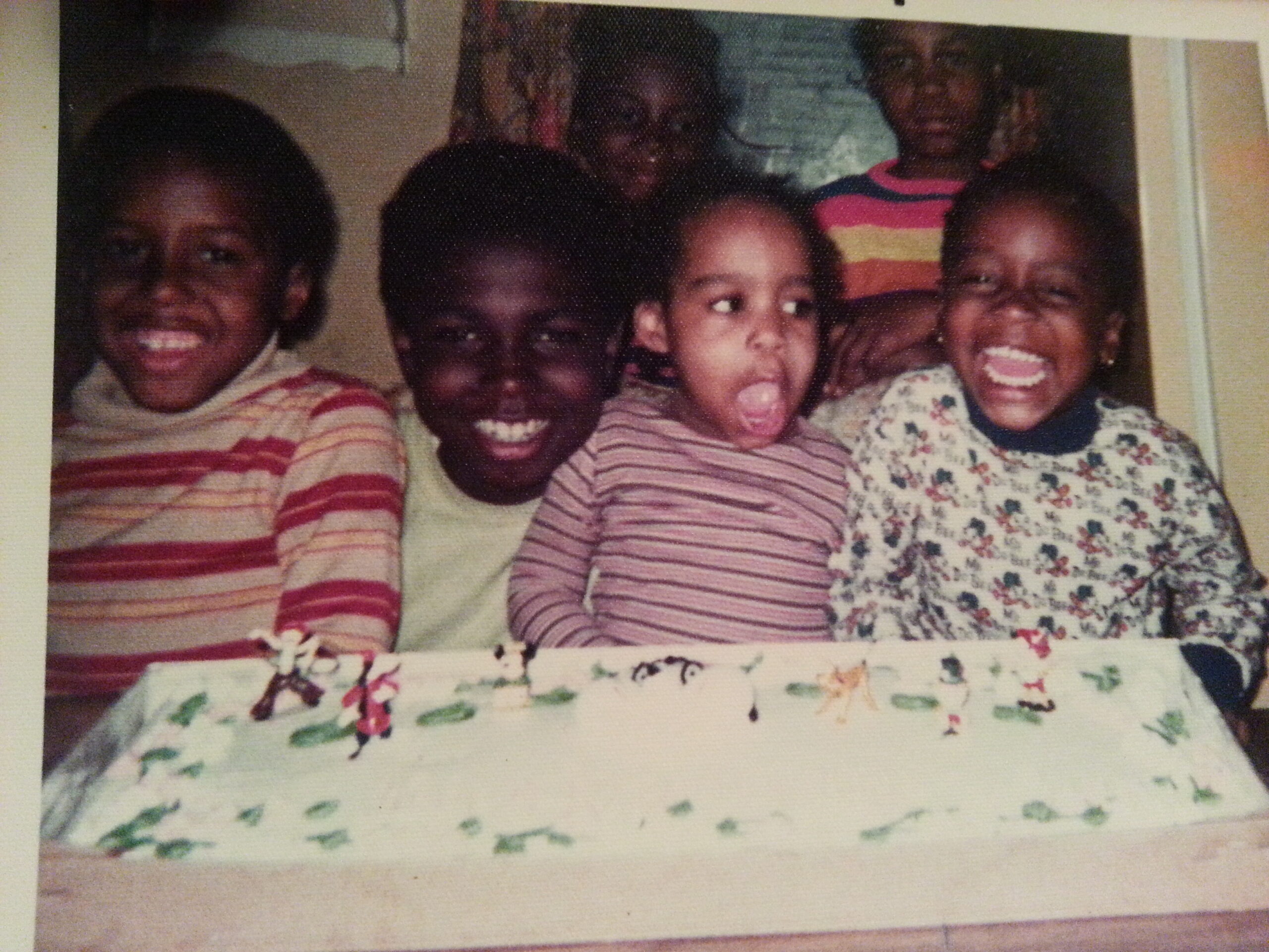 Five children gathered around a table with a decorated cake, smiling at the camera.