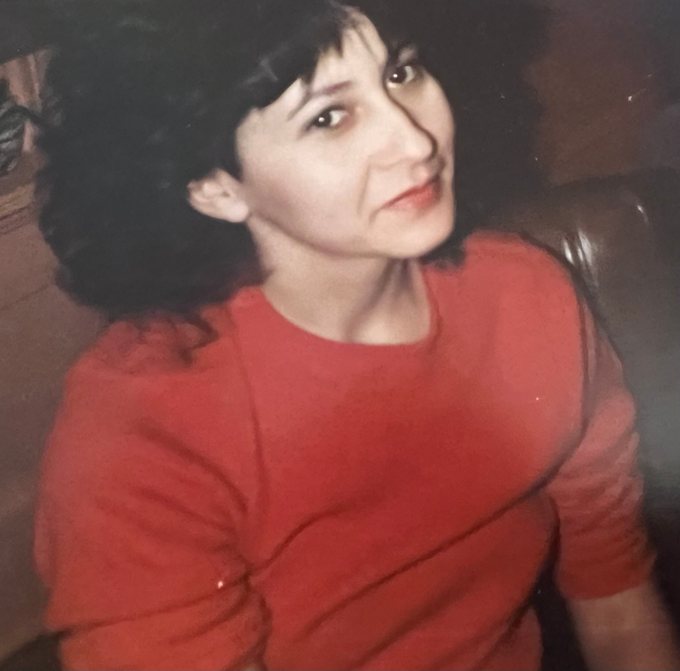 Close-up of a person with short dark hair wearing a red shirt, looking to the left.