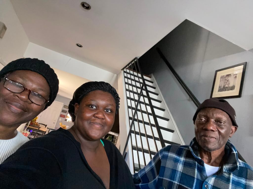 Three people posing for a casual selfie in a home, smiling at the camera by a staircase.