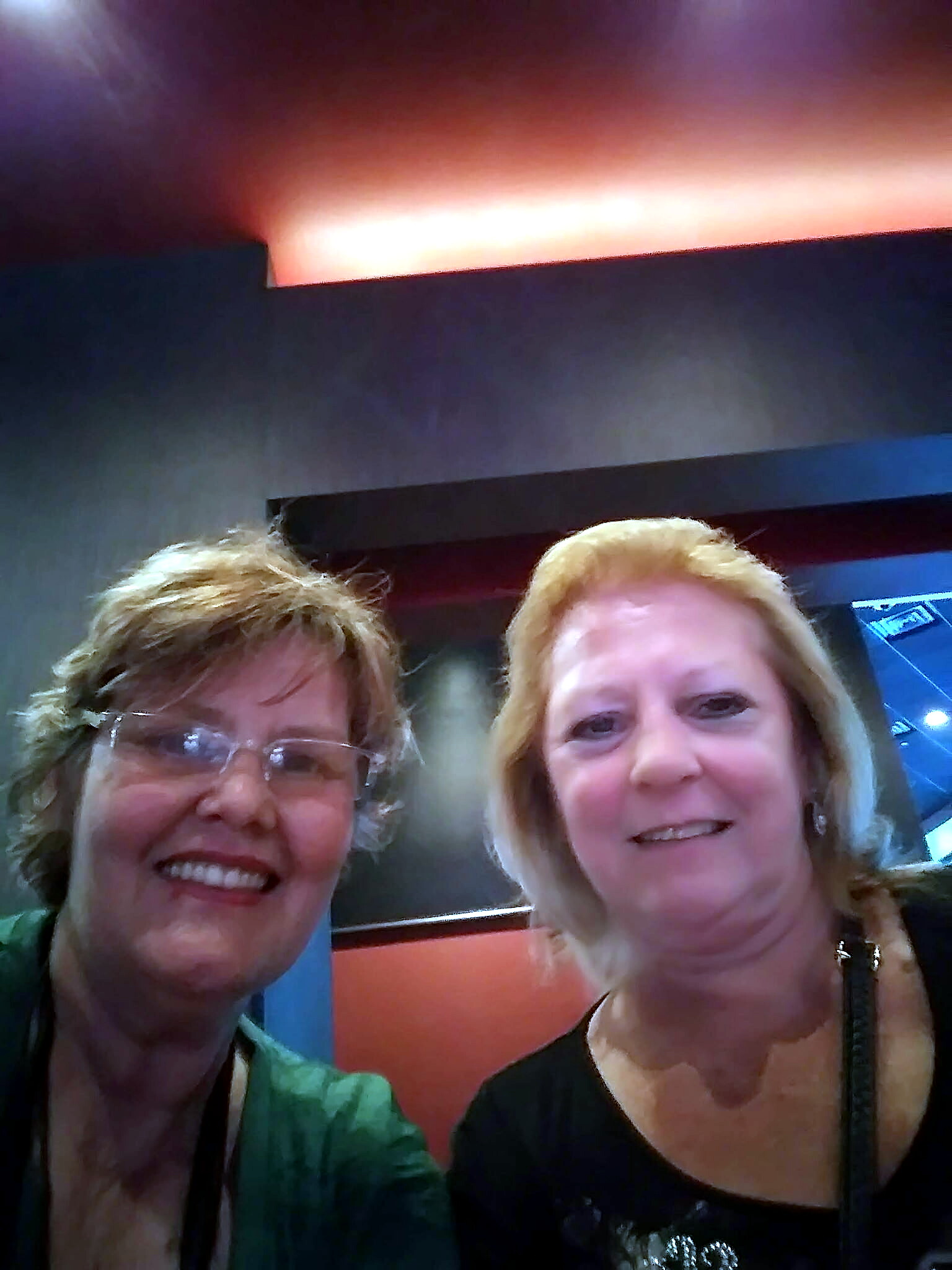 Two women smiling for a selfie in a dim, colorful indoor setting.