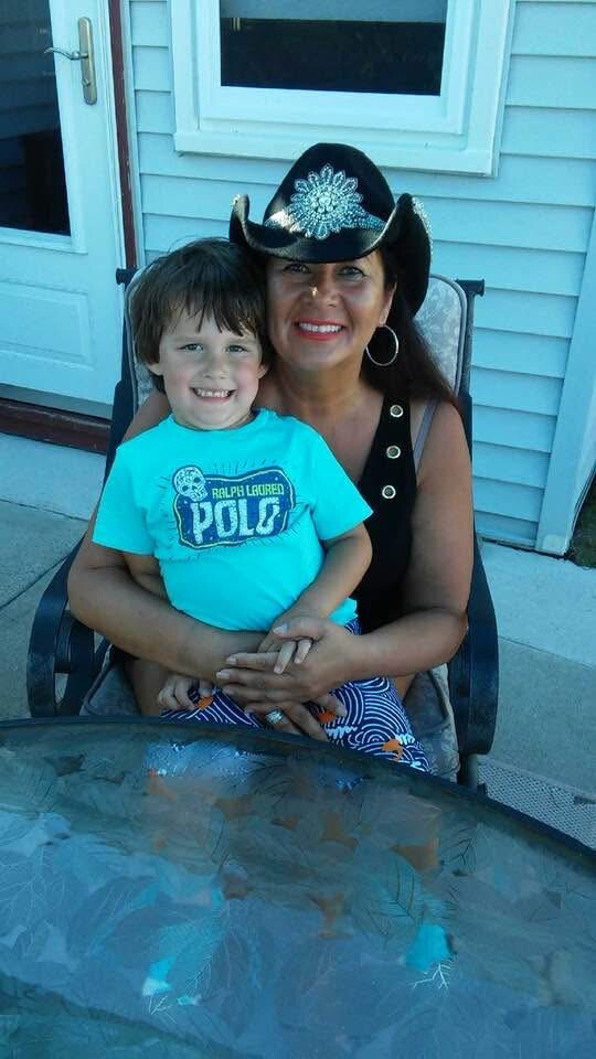 Smiling woman in a black cowboy hat with turquoise ornament sits with a smiling child on her lap outside a blue house patio door.