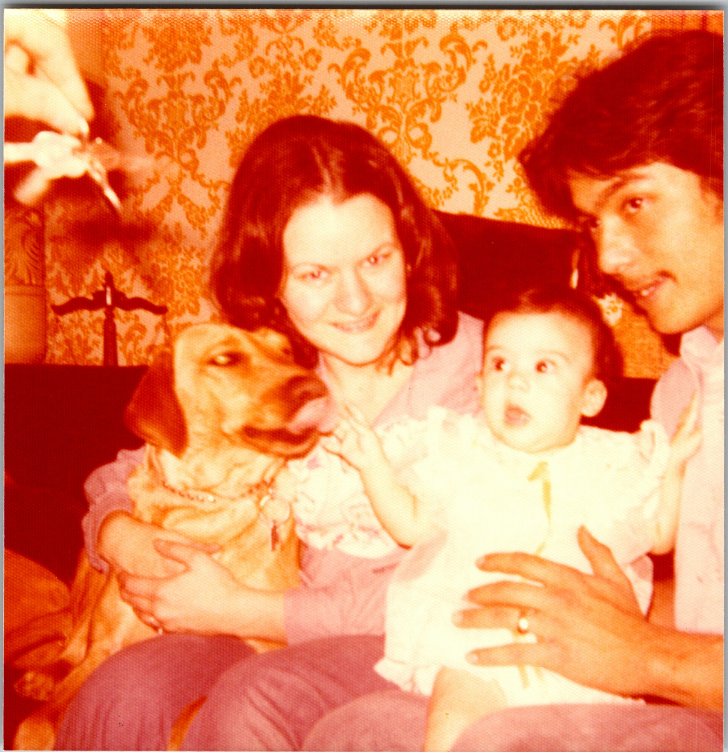 Group of smiling people posing together for a warm-toned family photo indoors with a patterned wallpaper backdrop.