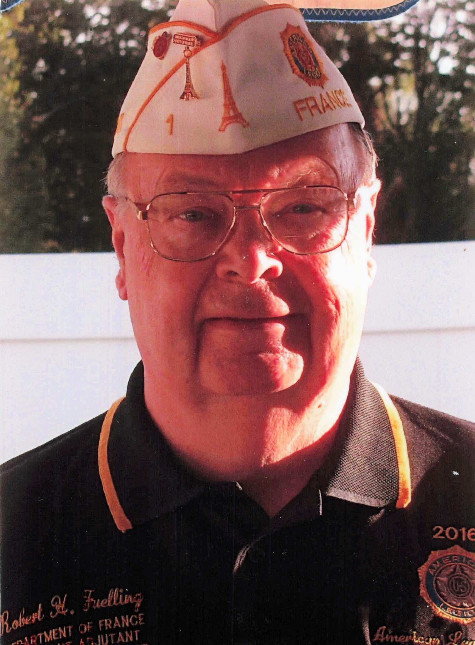 Close-up of an elderly man wearing a white France-themed hat with Eiffel Tower graphics on it.