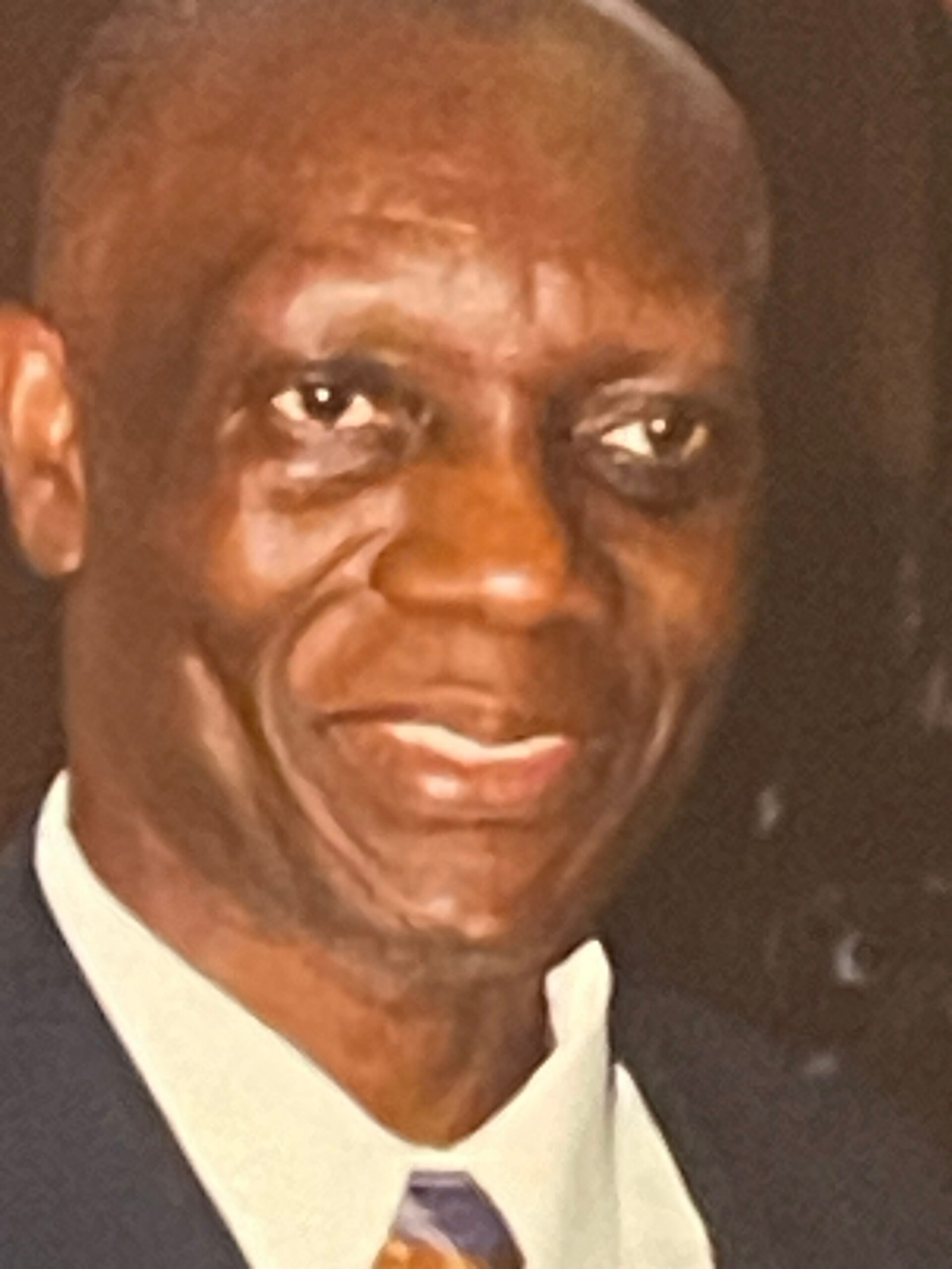 Close-up of a man wearing a dark suit and white shirt, shown from the chest up in a formal portrait.