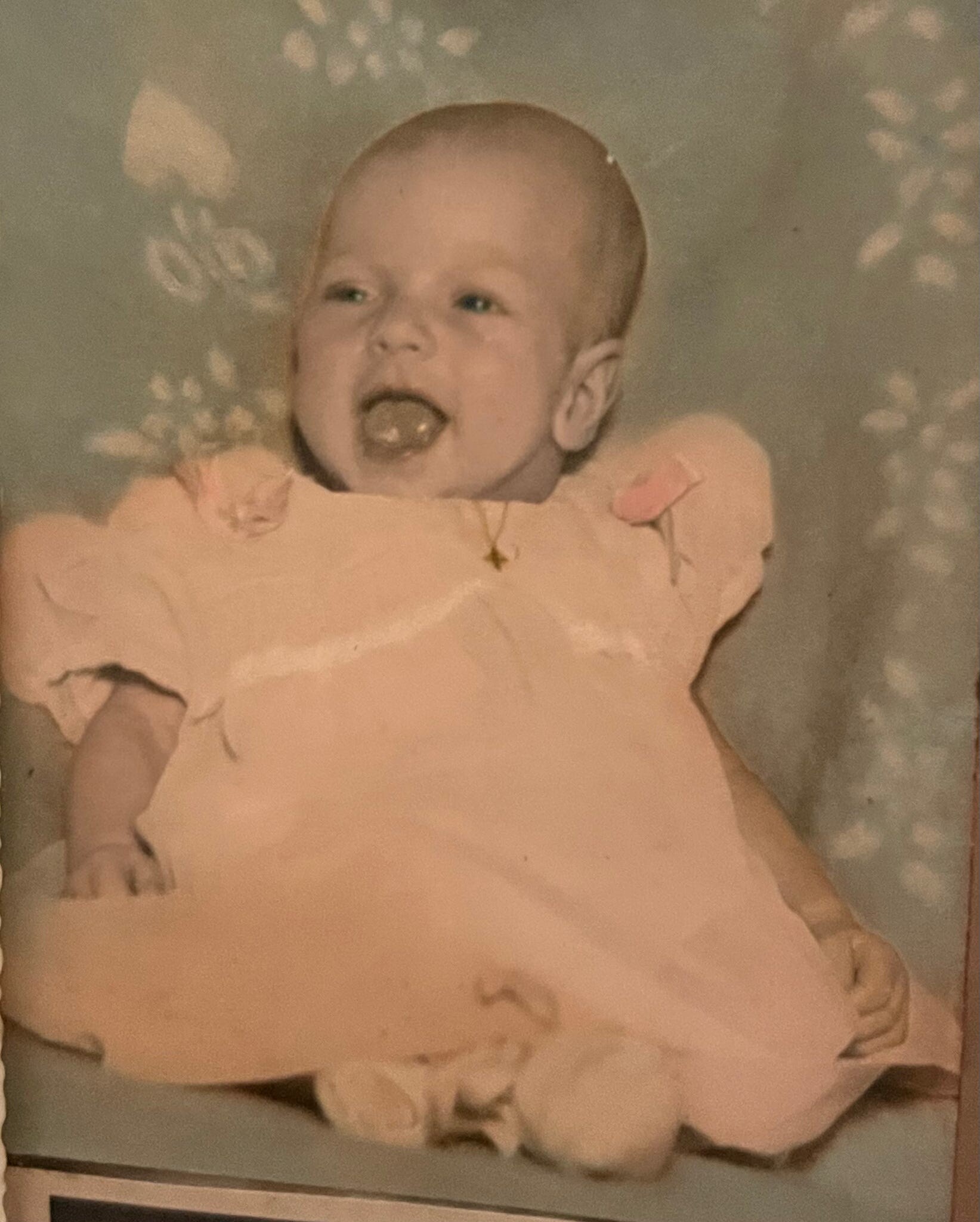 Close-up of a baby in a pink outfit with mouth open, looking to the left.