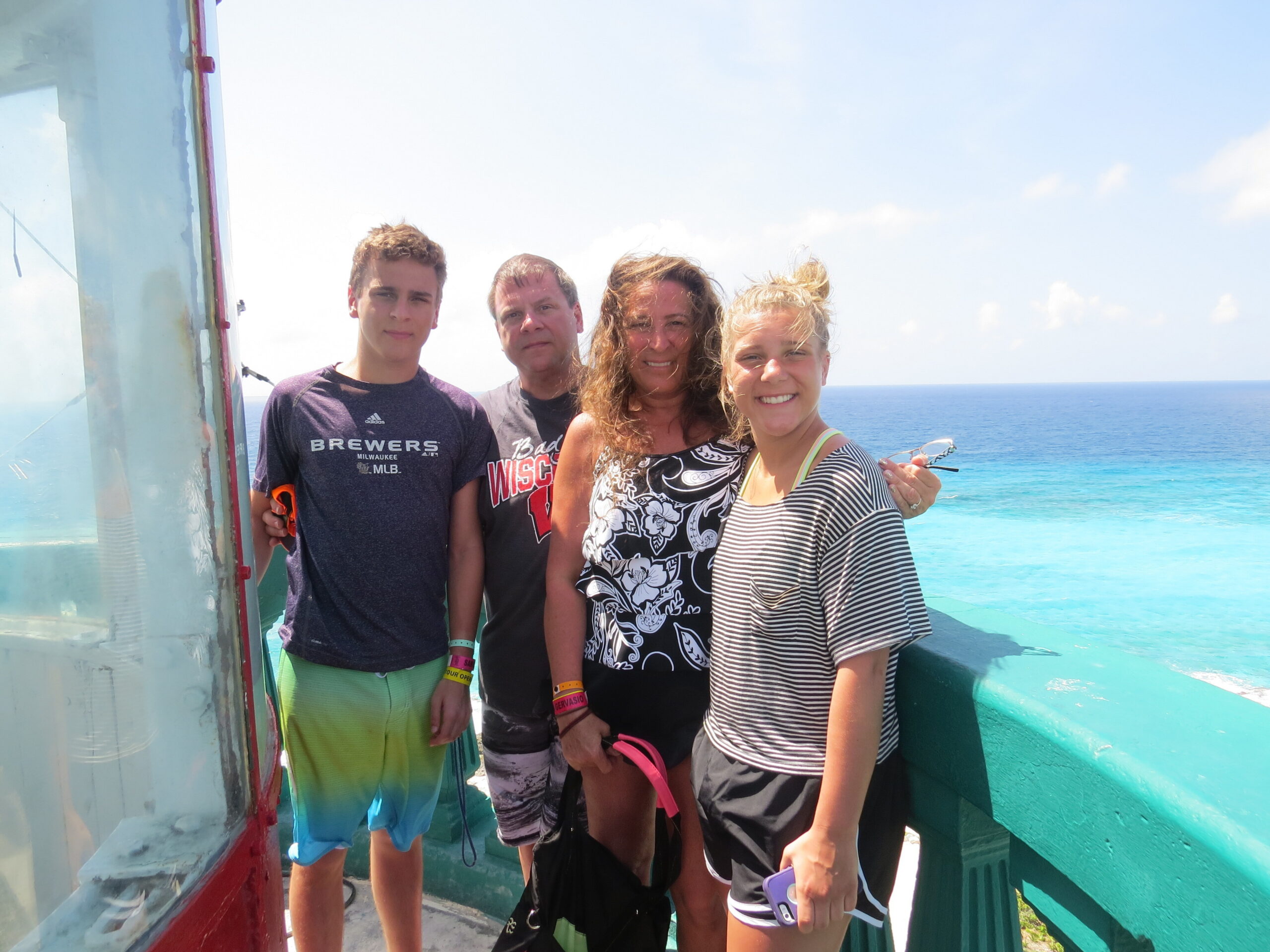Four people stand close together on a boat deck with the blue sea and sky behind them, smiling for a photo.