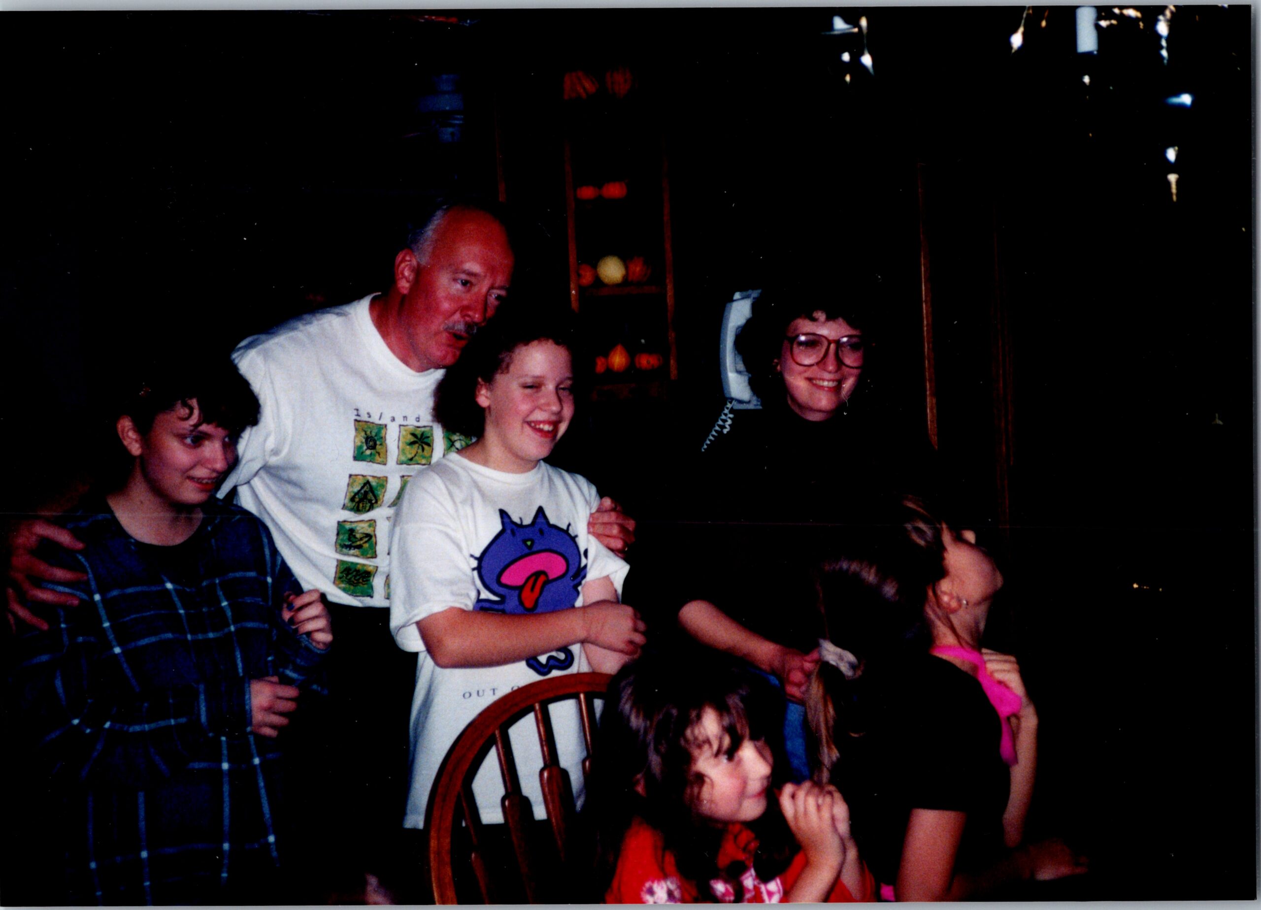 A man with a mustache and several children pose together in a dim room, with shelves of fruit visible in the background.