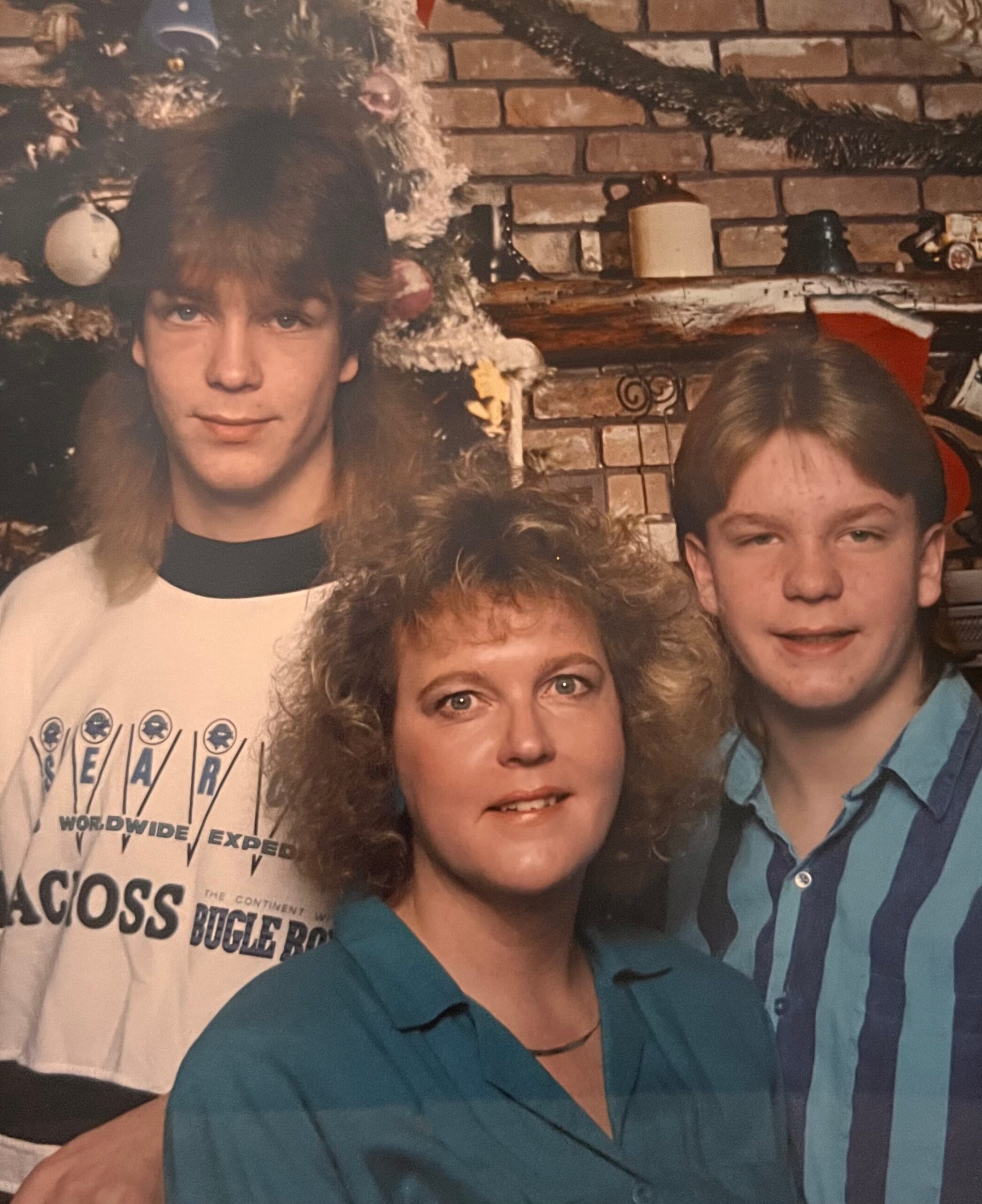 Family group photo taken in a living room with a brick fireplace and Christmas tree in the background, everyone wearing casual clothing.