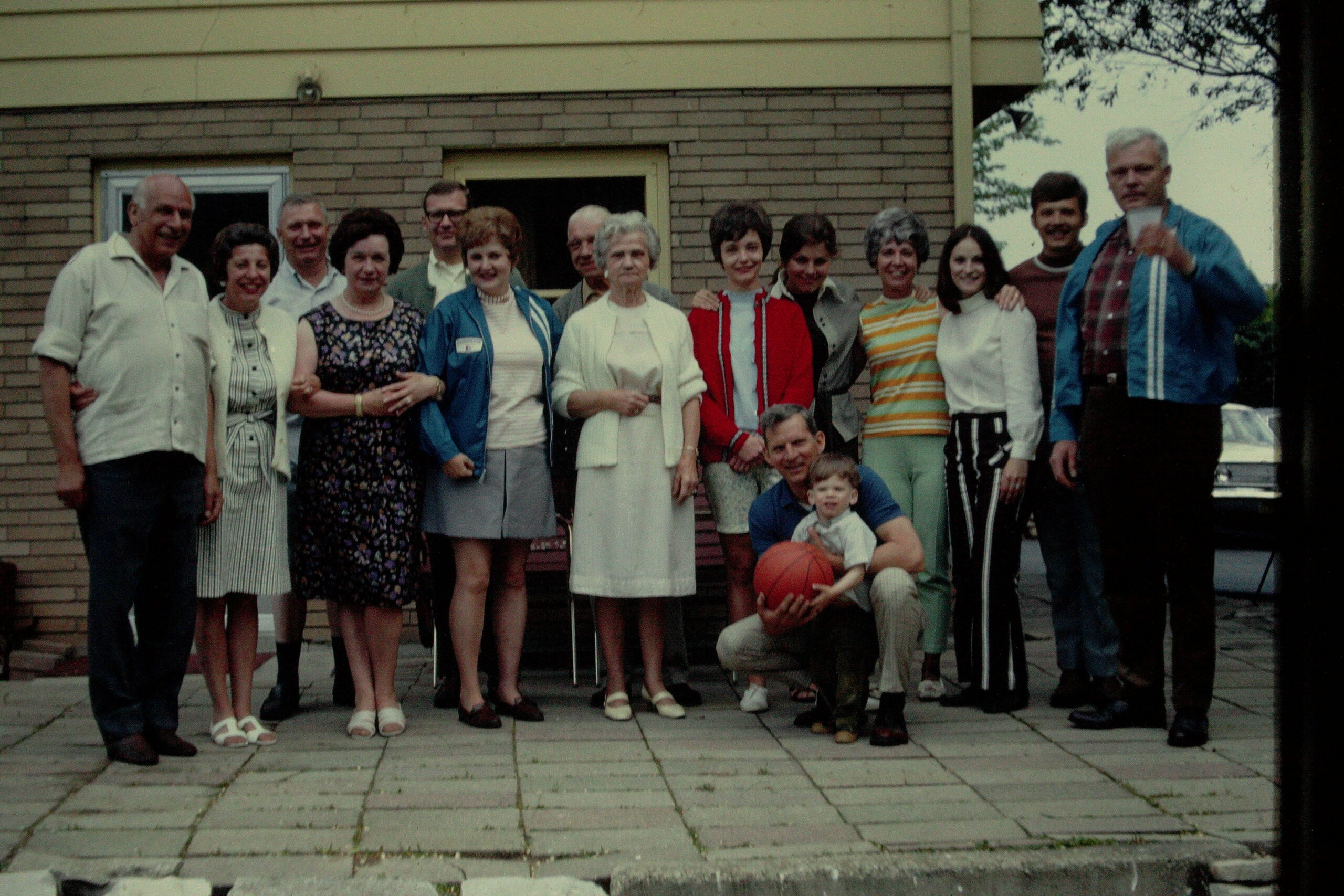 Group of adults posing together outside a brick building, with a child holding a basketball at the front.