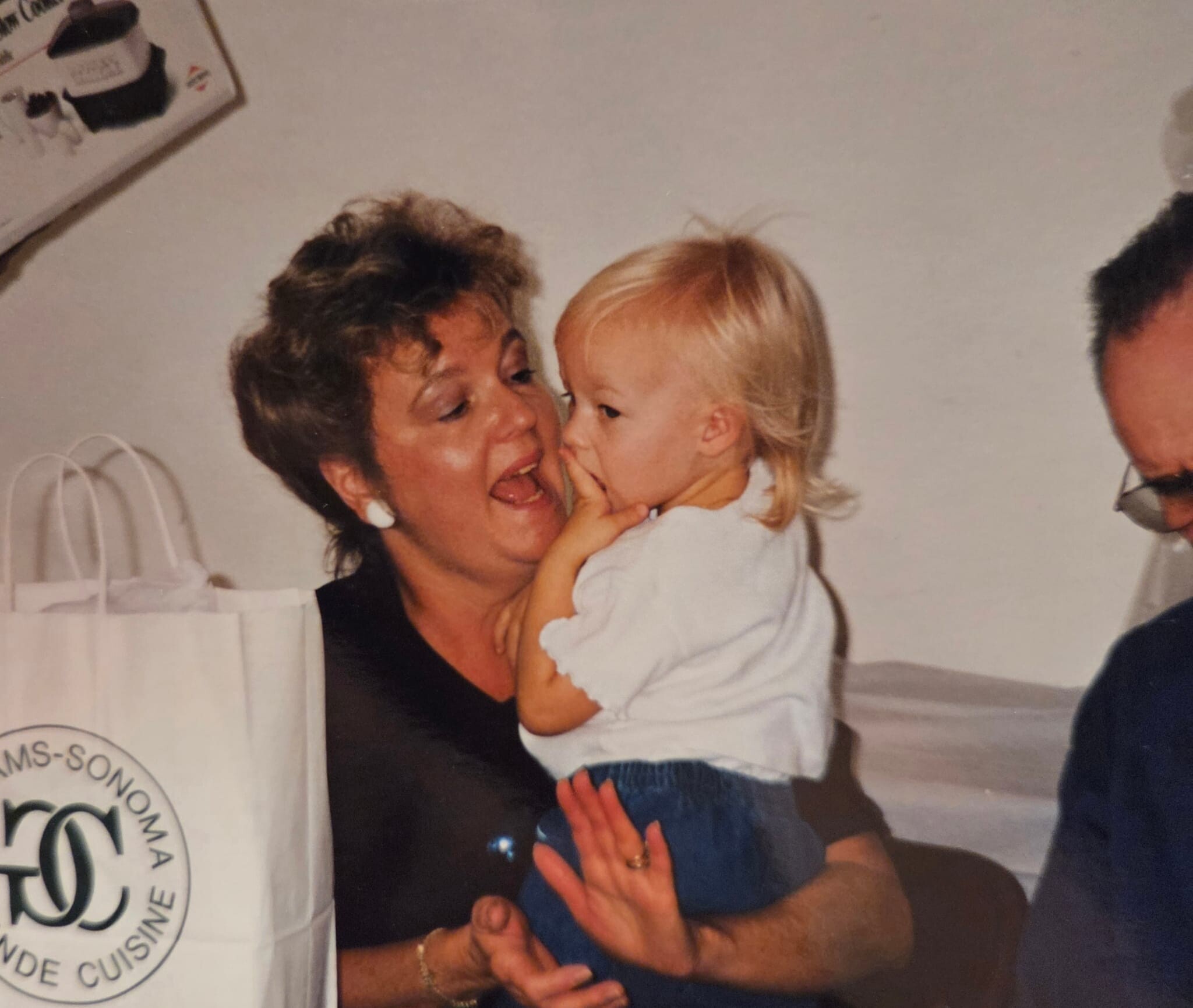Older woman holding a baby and sharing a kiss in a home setting, both facing each other with smiles visible.
