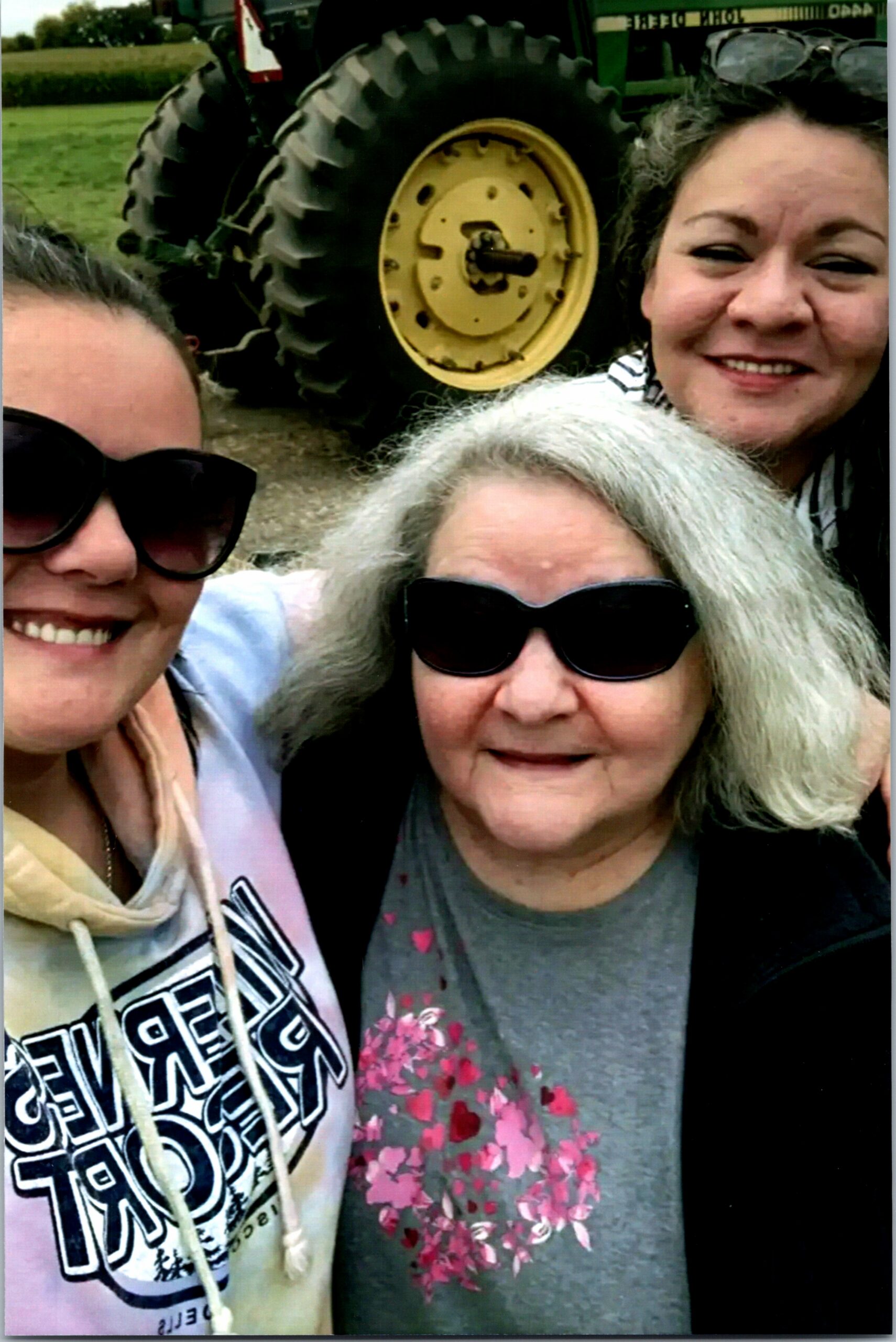 Three smiling women taking a selfie outdoors with a tractor tire in the background.