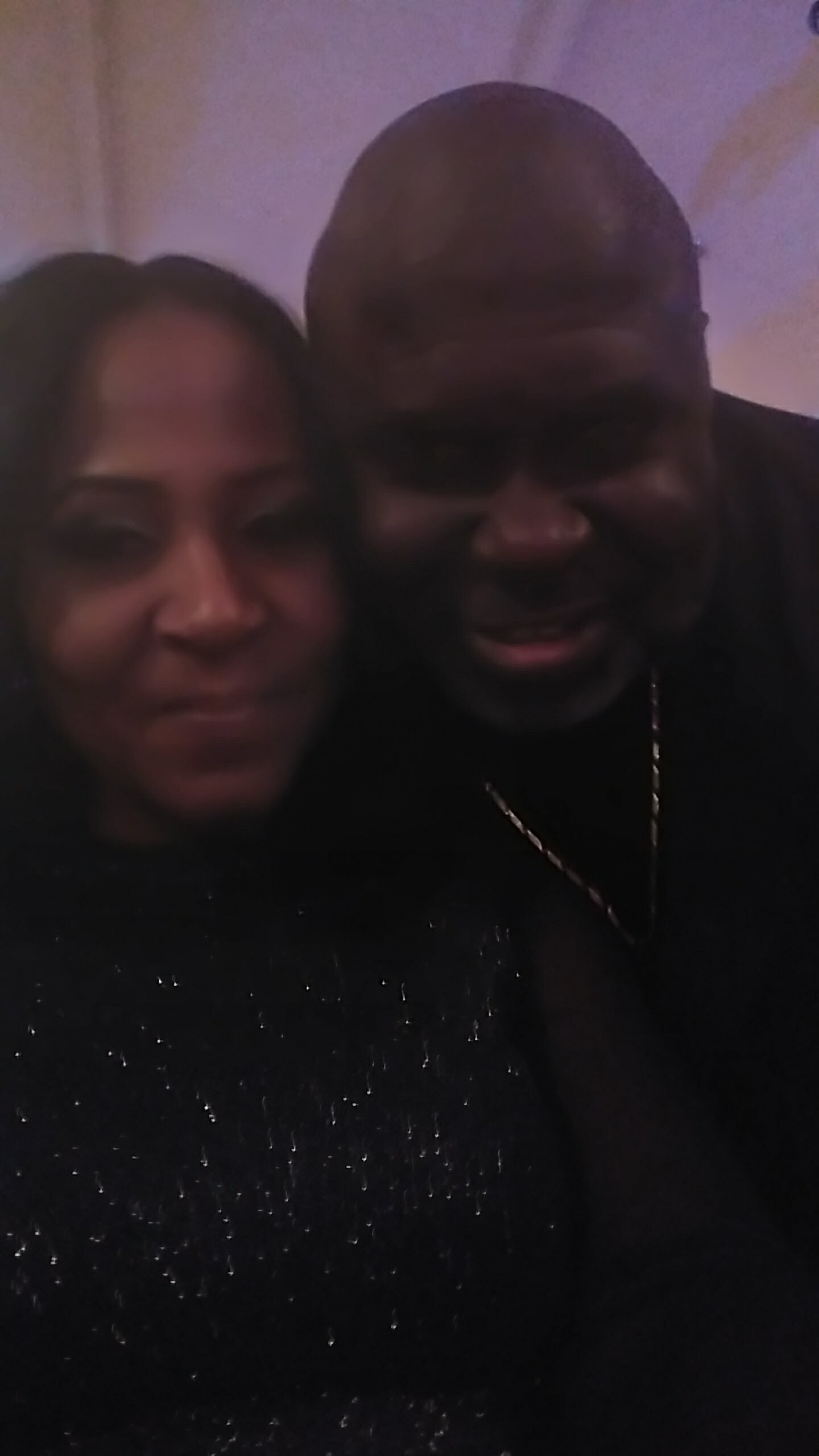 Close-up selfie of a smiling couple posing together in a dimly lit setting.