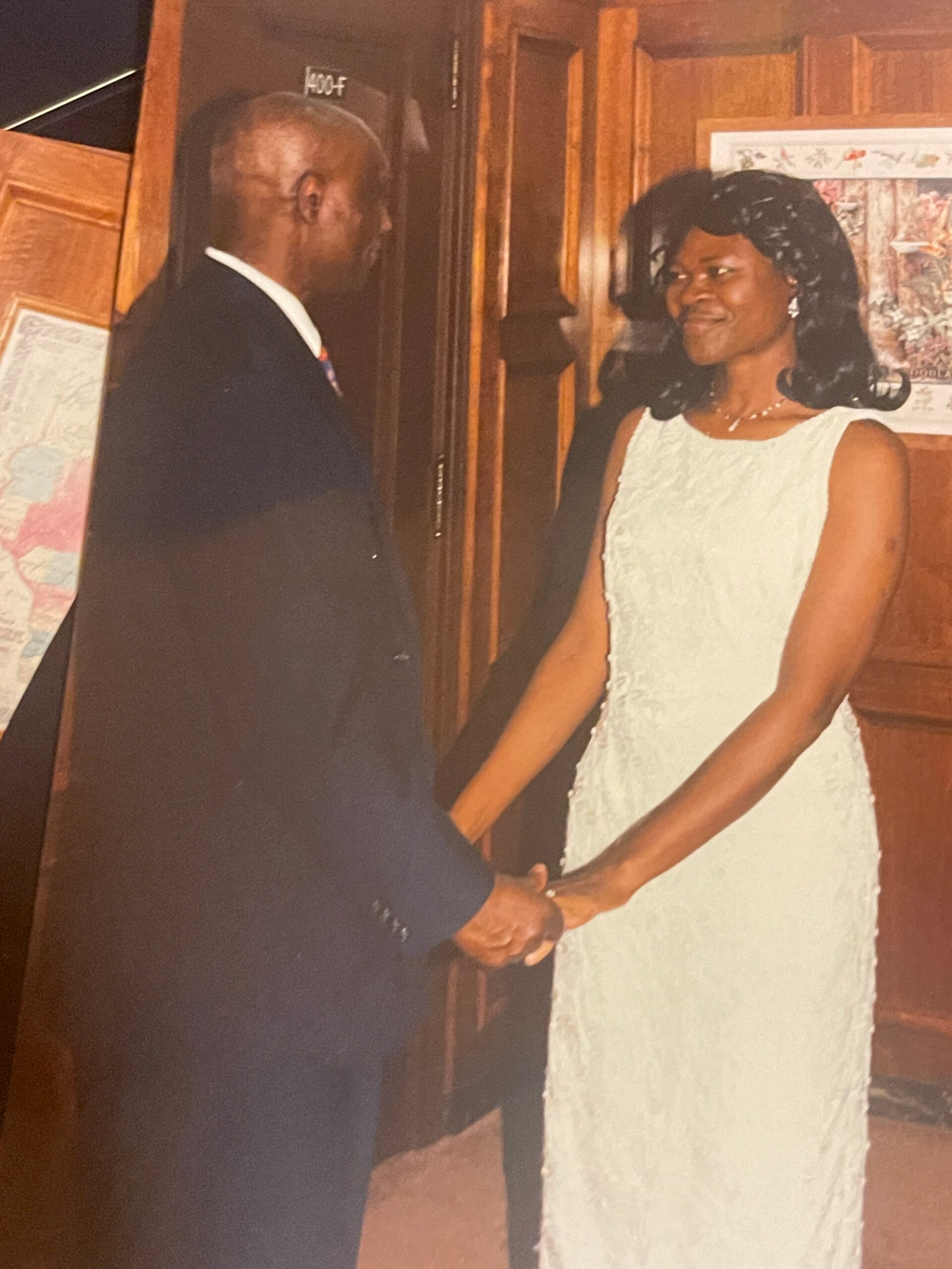 Bride in a white wedding dress and groom in a dark suit hold hands and smile at each other in a wooden interior.