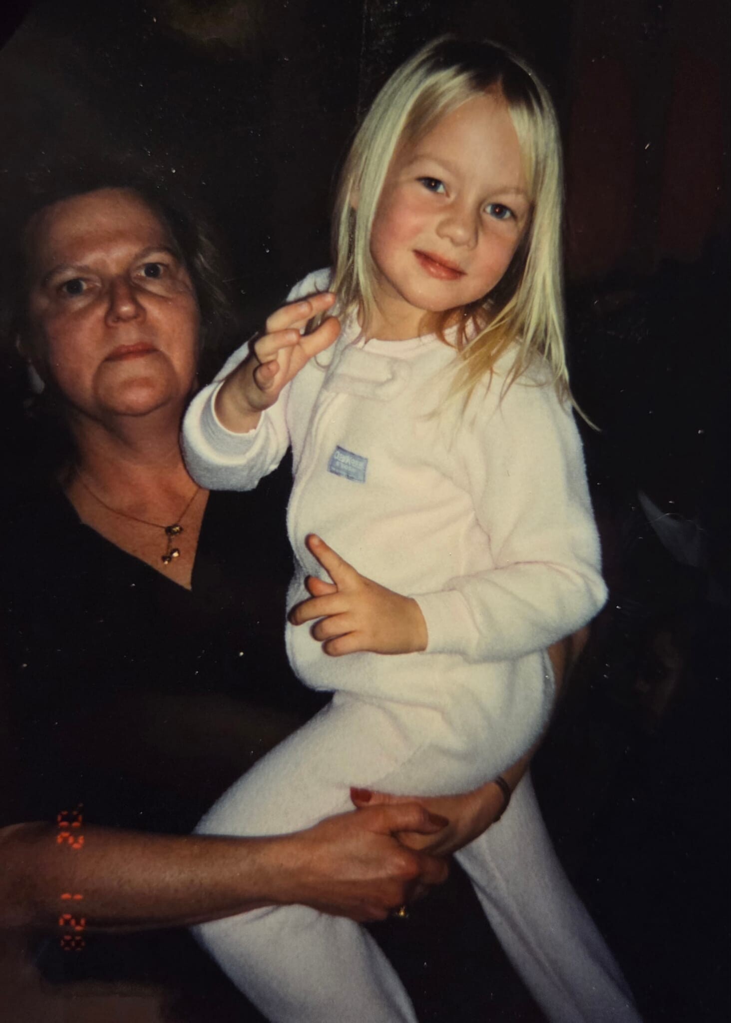 Grandmother holding a smiling young girl in white pajamas, posing for a photo indoors