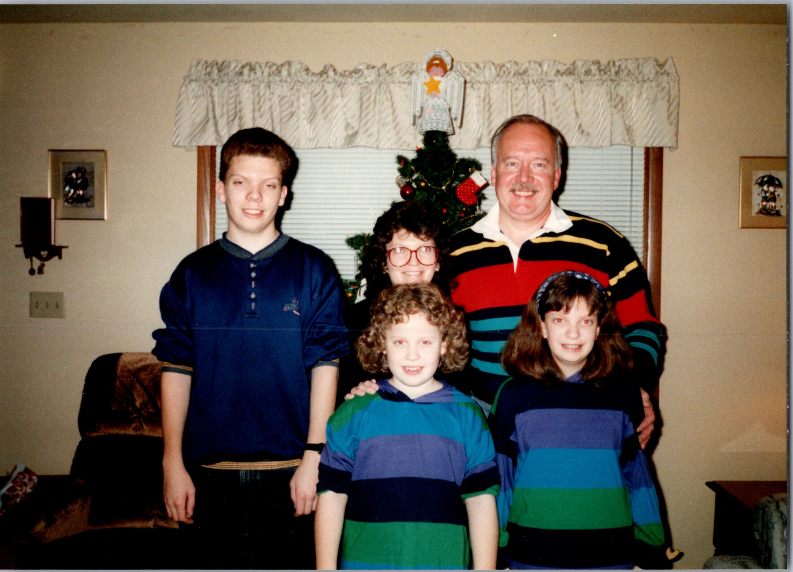 Family of six posing for a Christmas photo in a living room, with a decorated tree behind them.