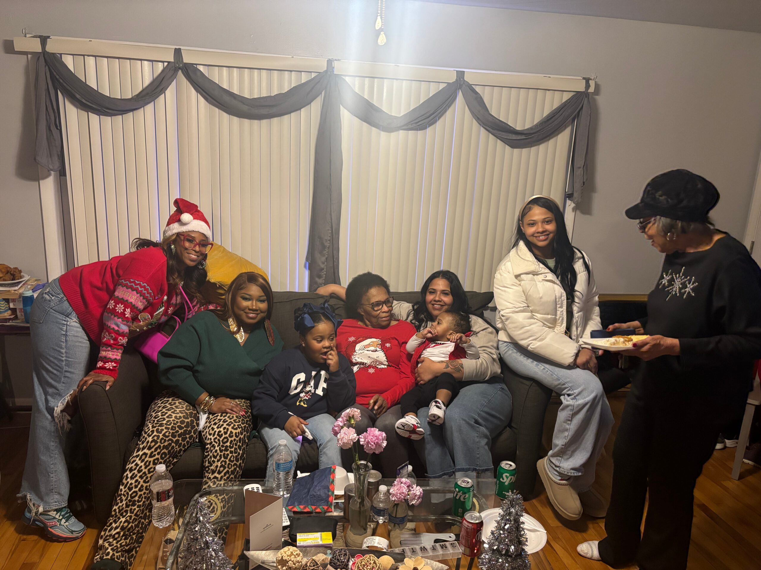 Group of people at a Christmas party posing on a sofa, with snacks and drinks on a glass coffee table in front of them.