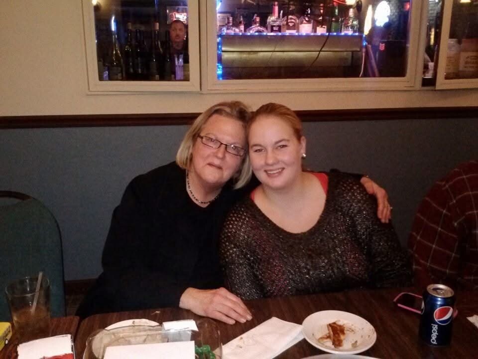 Two women sit together at a restaurant table, smiling, with drinks and plates in front.