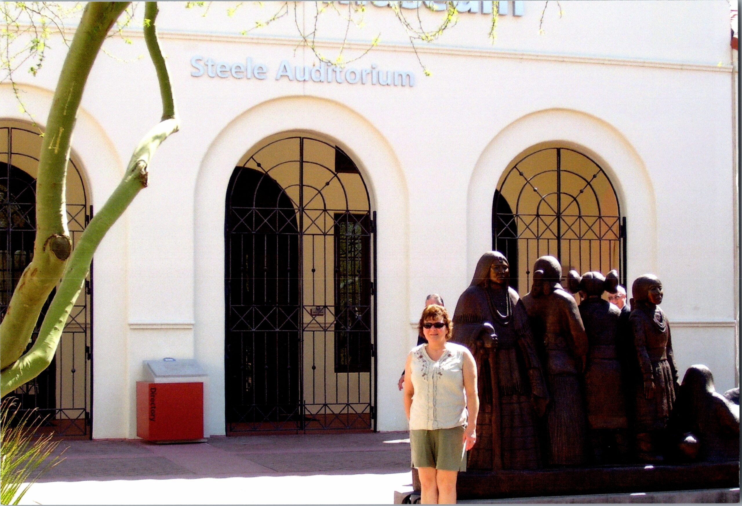 Exterior view of Steele Auditorium with arched windows and a row of statues; a woman in a light blouse stands in front.
